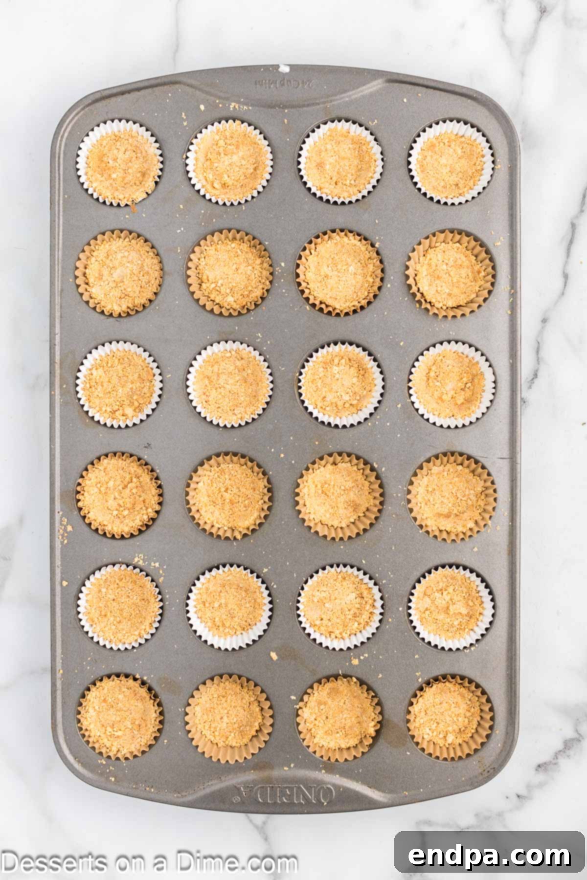 Mini muffin tin with graham cracker crust pressed into each liner.