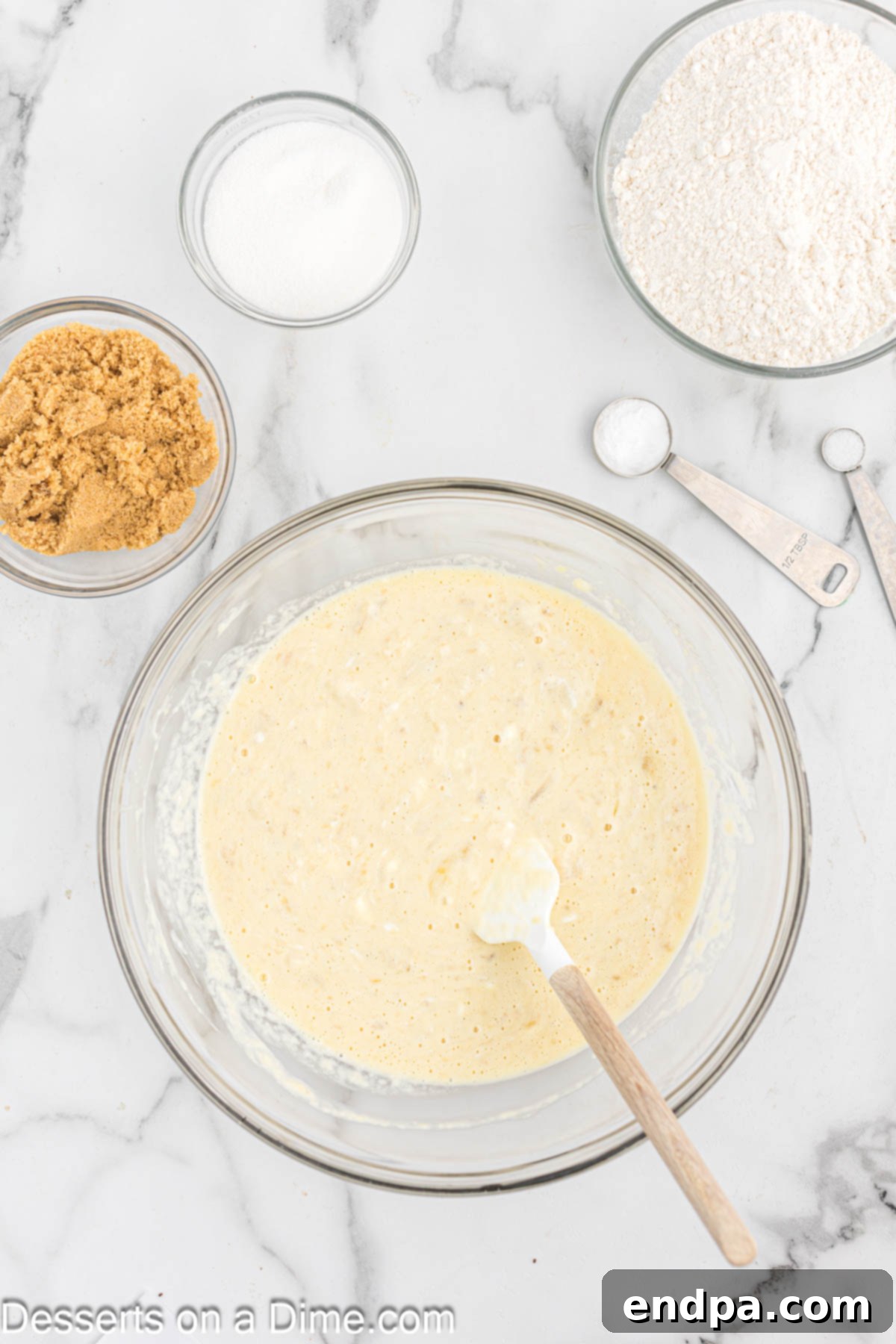 Large mixing bowl containing mashed bananas and other wet ingredients, partially mixed.