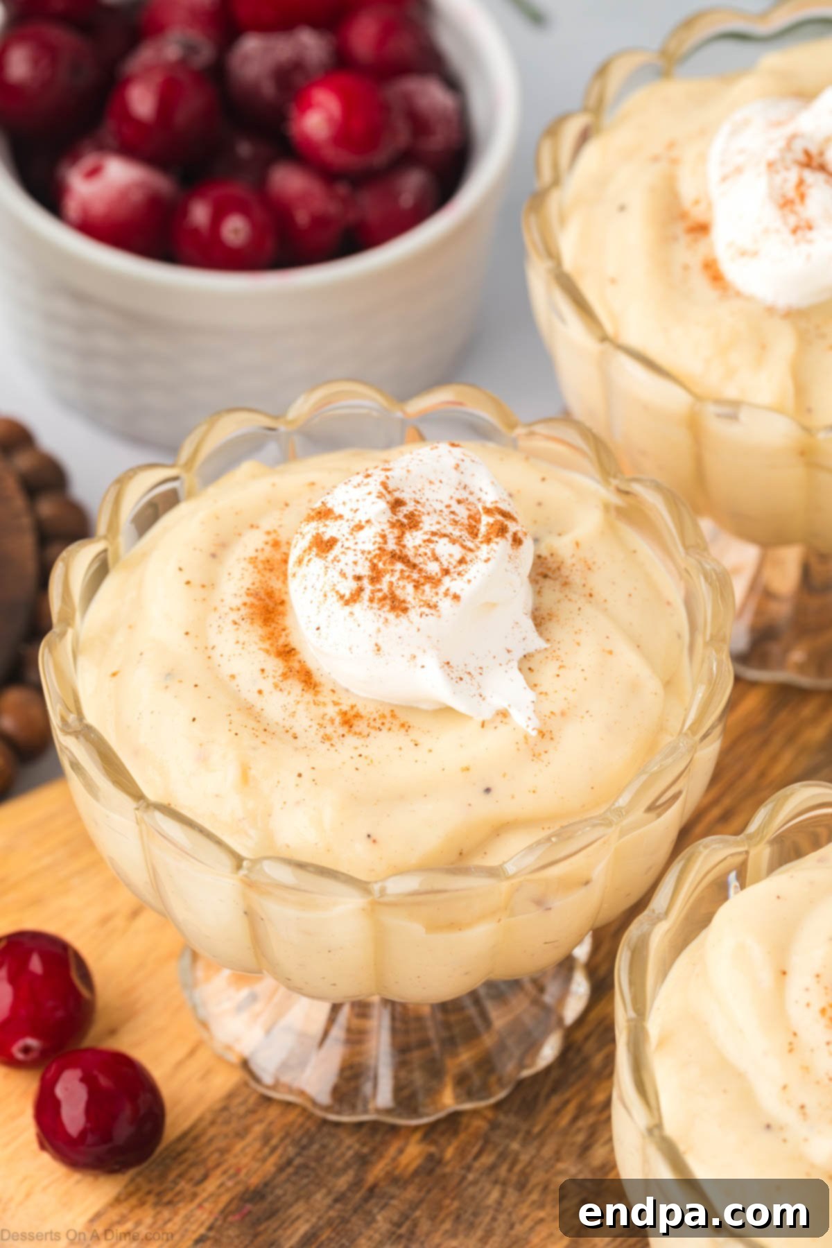 Two glass bowls filled with golden homemade eggnog pudding, generously topped with fluffy whipped cream and a sprinkle of ground cinnamon, ready to be enjoyed as a festive holiday dessert.