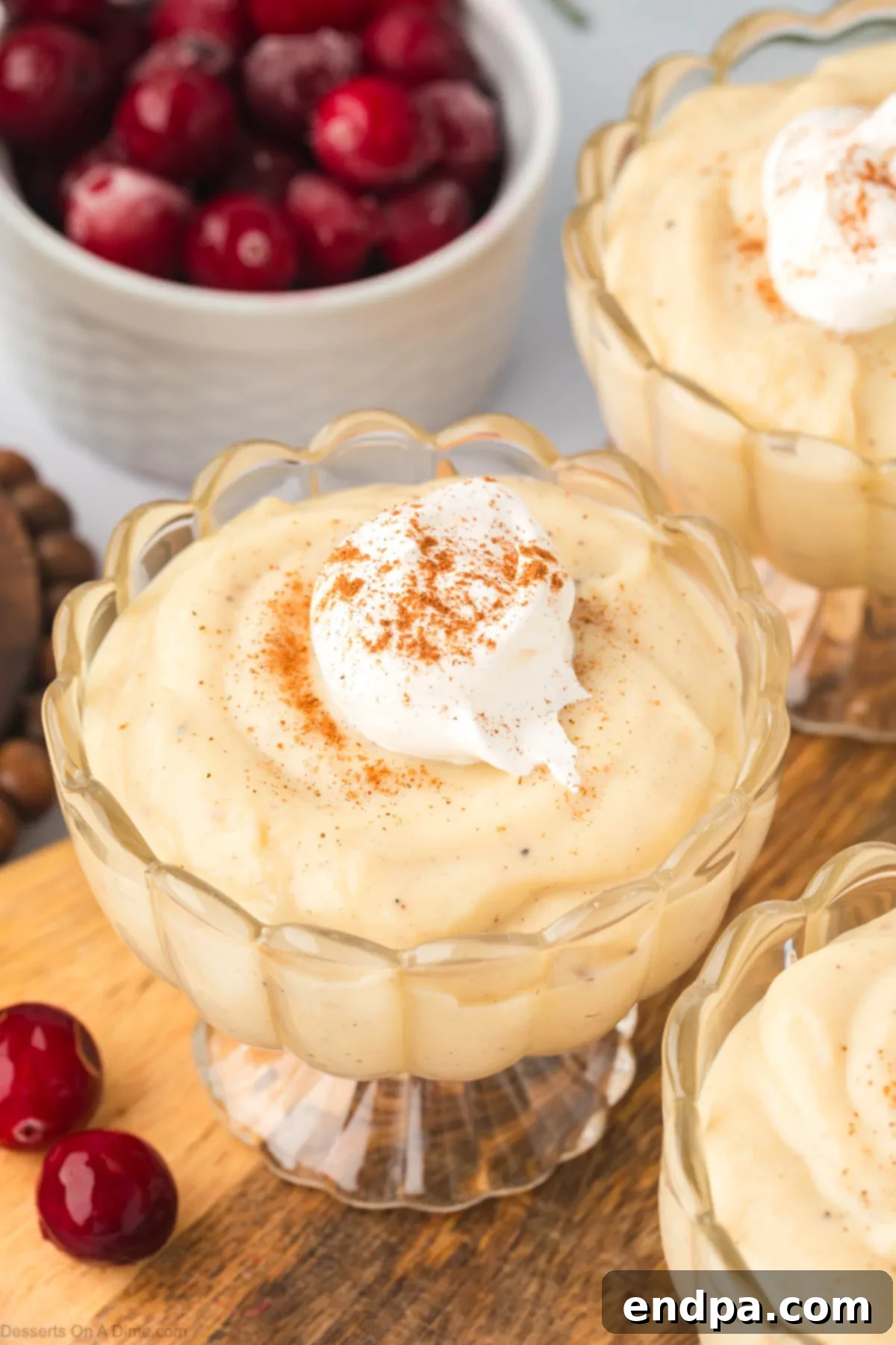 A beautifully presented single serving of creamy eggnog pudding in a glass bowl, topped with a generous swirl of whipped cream and a sprinkle of ground cinnamon, inviting indulgence.