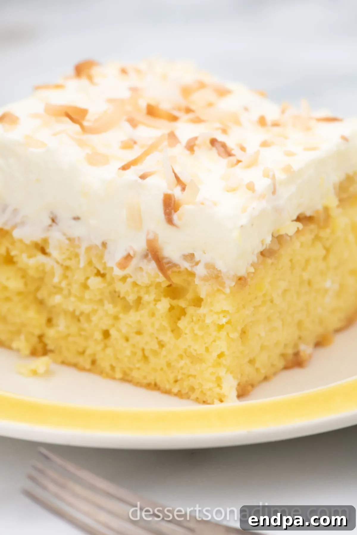 A delectable slice of Hawaiian Wedding Cake served on a white plate, showcasing its moist layers and generous toppings of pineapple, creamy frosting, and toasted coconut.