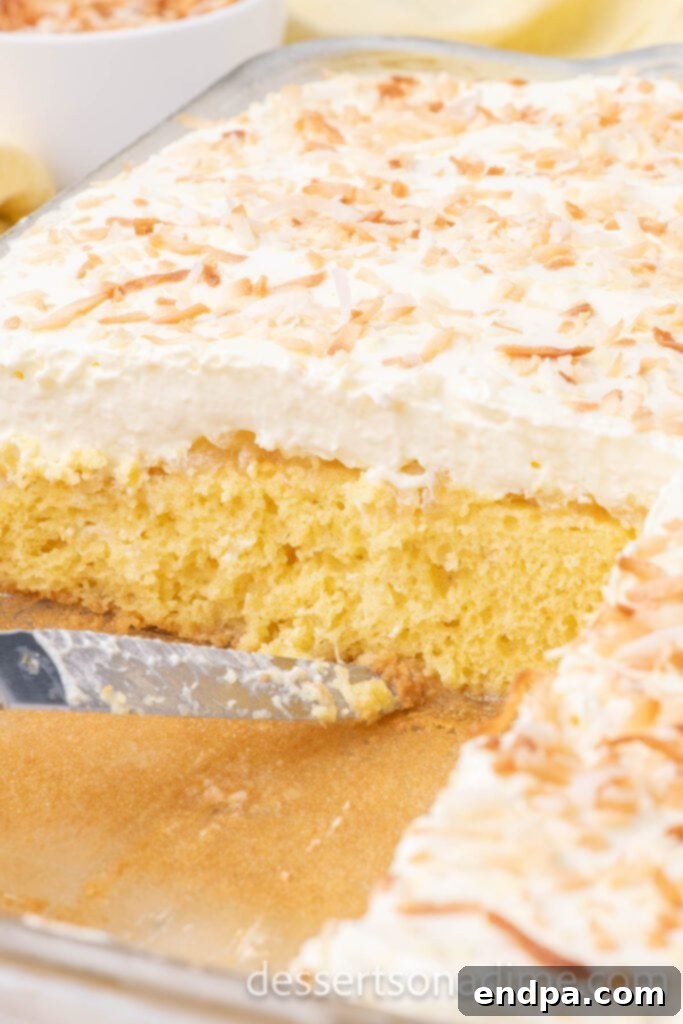 A large Hawaiian Wedding Cake, beautifully garnished with toasted coconut, being carefully cut into individual servings directly from its baking dish.