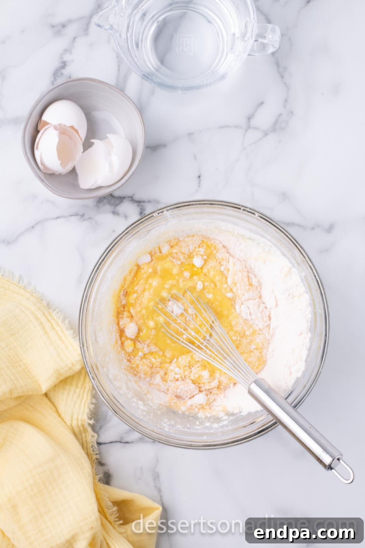 A large mixing bowl containing yellow cake mix ingredients being combined, preparing for the initial baking stage.