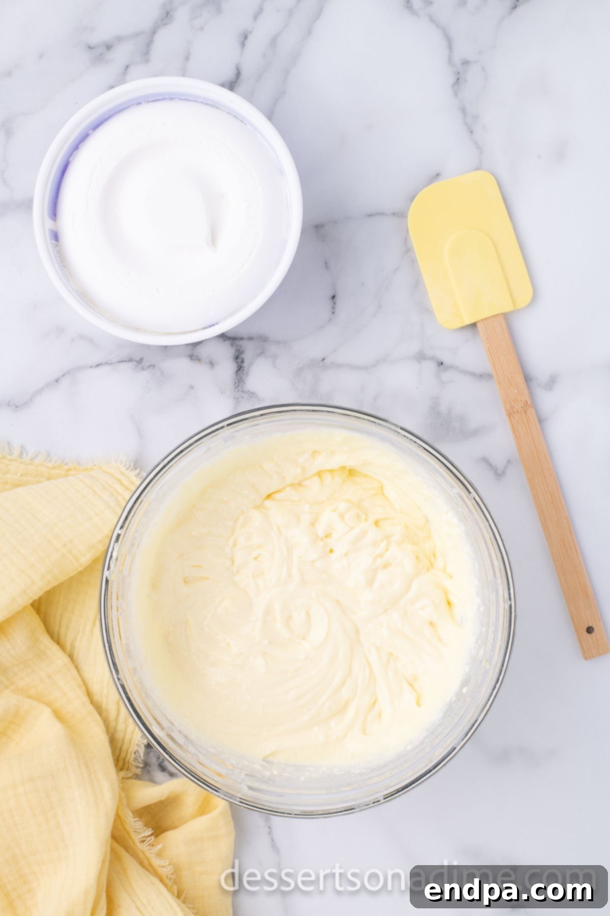 A mixing bowl containing dry instant vanilla pudding mix, cold milk, and softened cream cheese, being beaten to a smooth, creamy consistency.