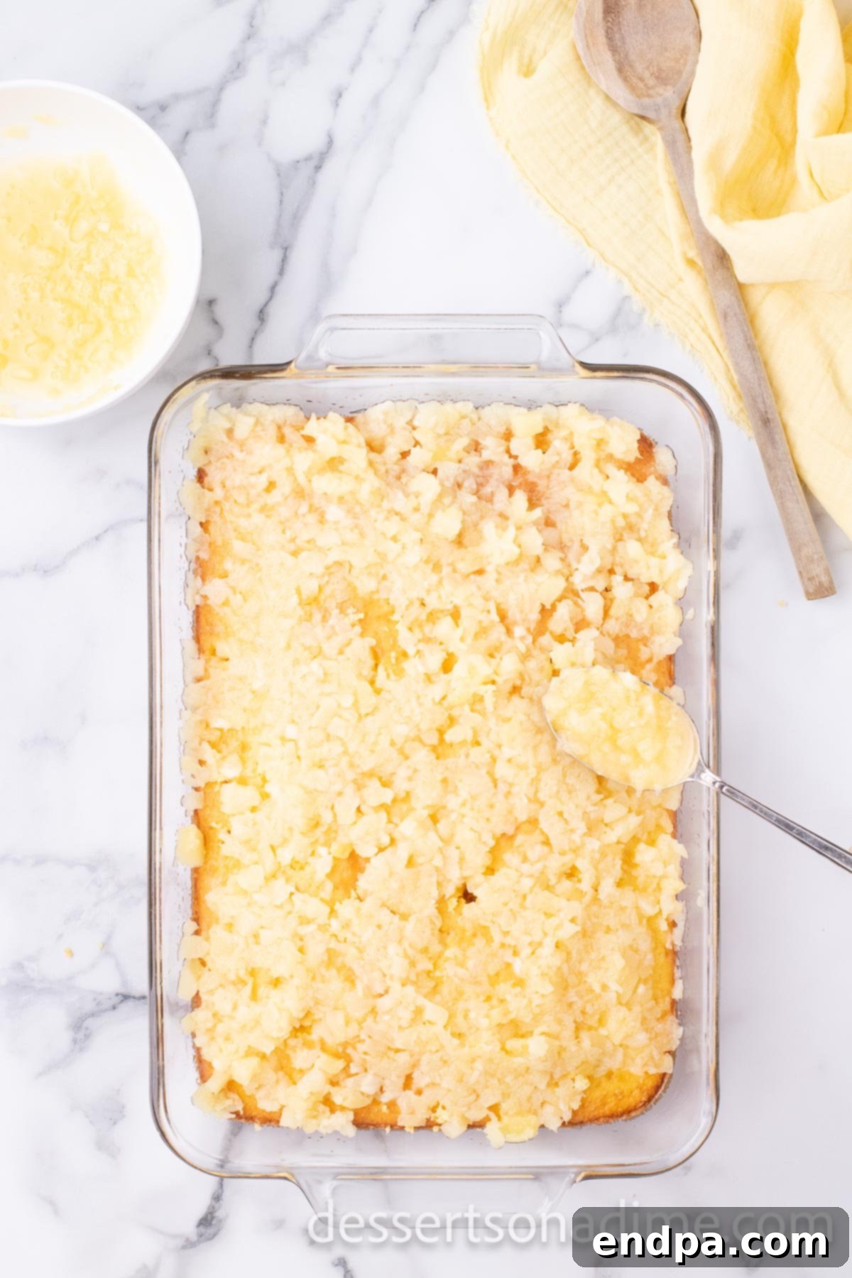Crushed pineapple, complete with its natural juices, carefully spread over the entire poked surface of the cake, ensuring every hole is filled.