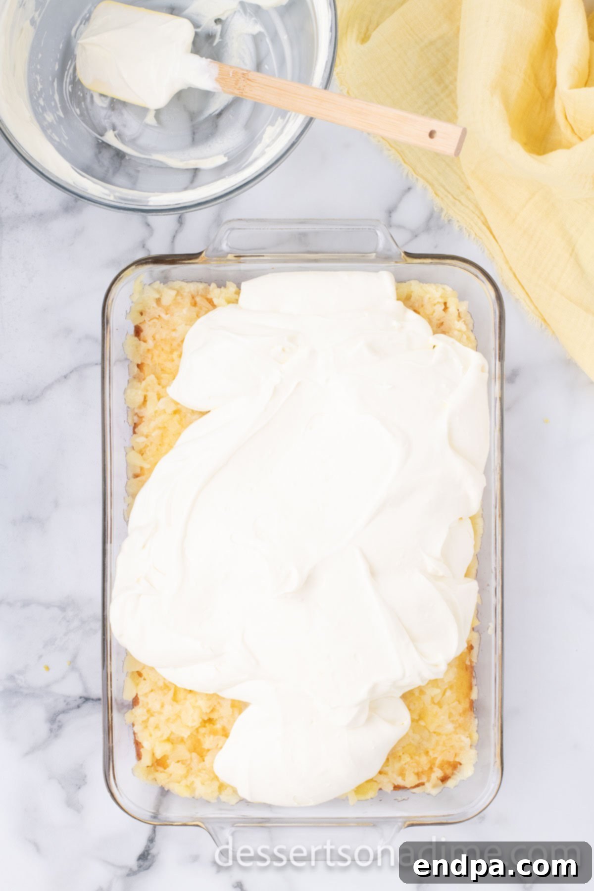 The creamy whipped topping and pudding mixture spread in a thick, smooth, and even layer over the pineapple-infused cake, creating a pristine white canvas.