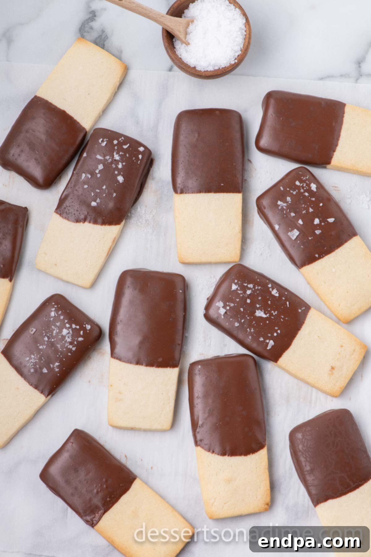 Hand sprinkling sea salt over a chocolate-dipped shortbread cookie.