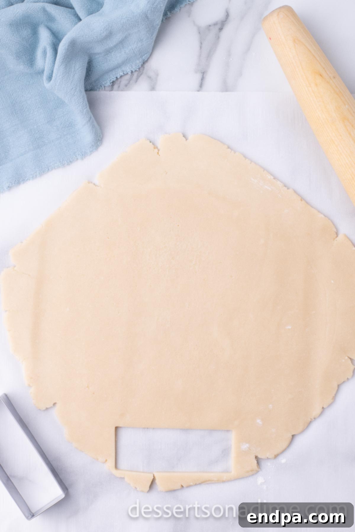 Shortbread cookie dough rolled out to an even thickness on parchment paper with a rolling pin.