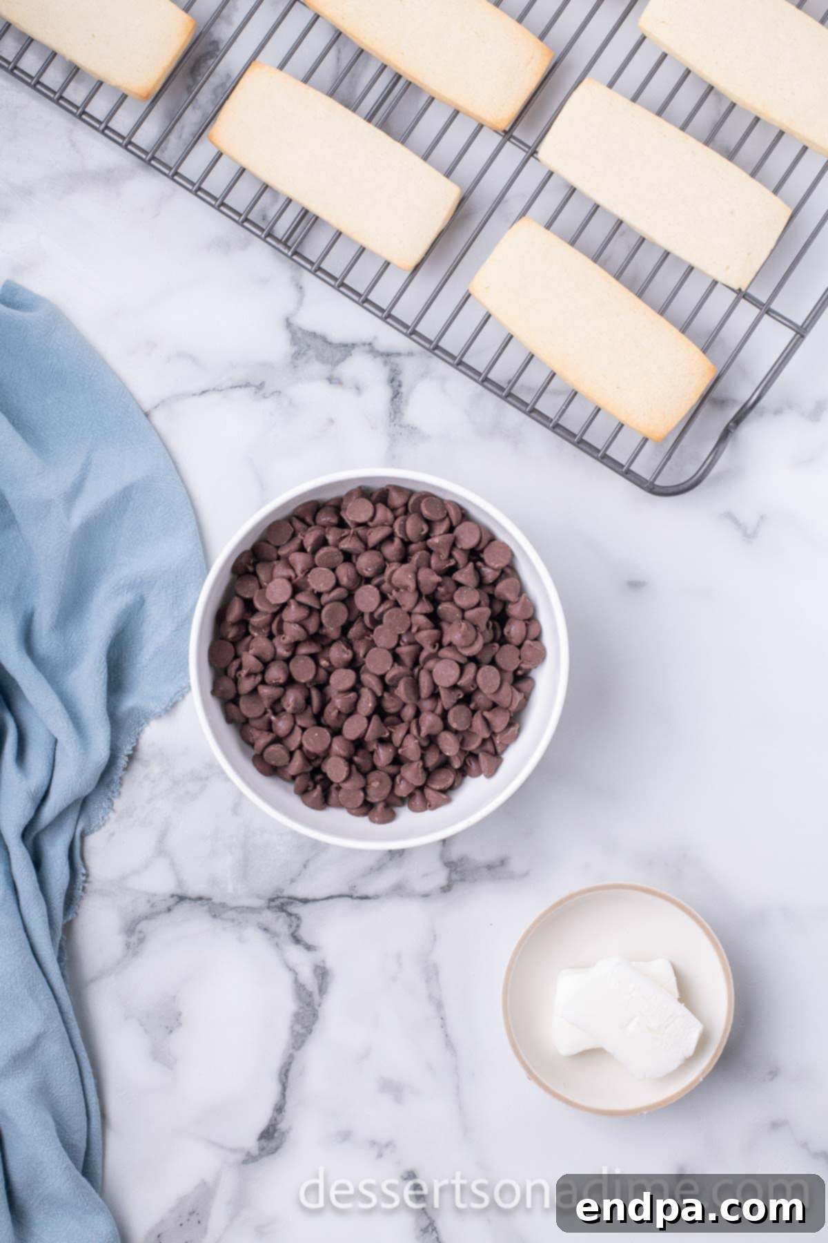 Bowl of chocolate chips beside baked shortbread cookies cooling on a wire rack.
