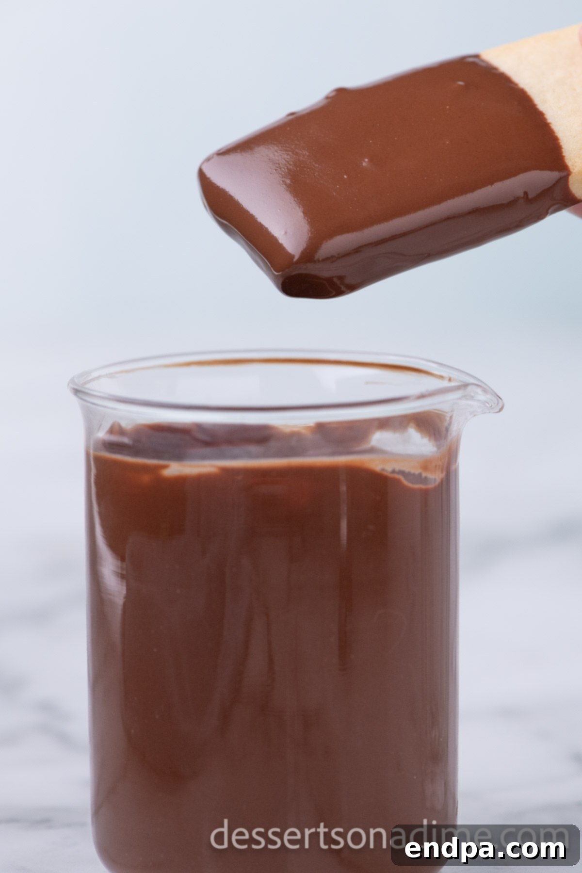 A shortbread cookie being carefully dipped into a bowl of smooth, melted chocolate.