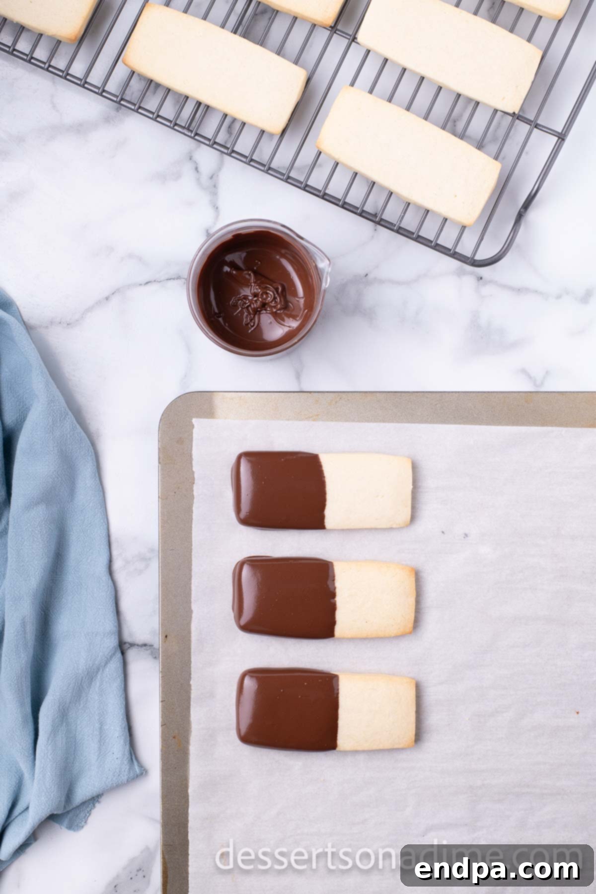 Several shortbread cookies, half-dipped in chocolate, resting on a baking sheet to set.