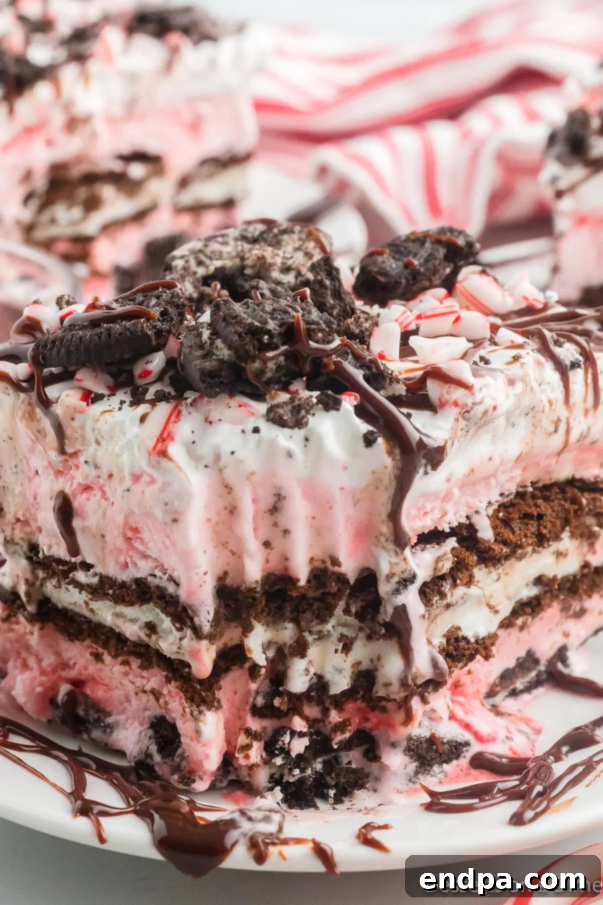 Holly Jolly Ice Cream Cake 12 A square slice of Christmas ice cream cake on a white plate with visible layers of cookies, ice cream, and toppings.