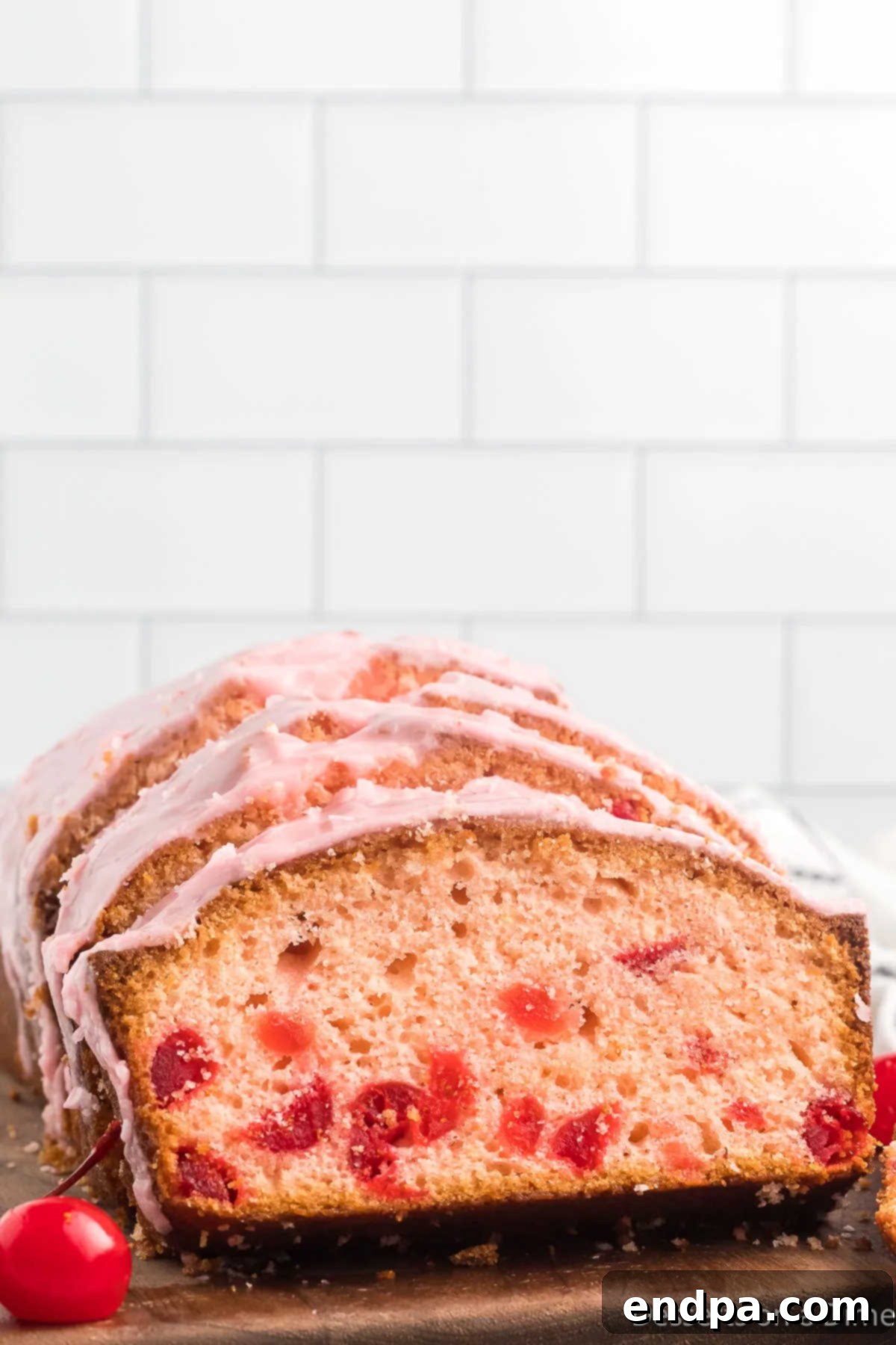 Loaf of cherry bread sliced on a cutting board, showing its vibrant pink interior and almond glaze.