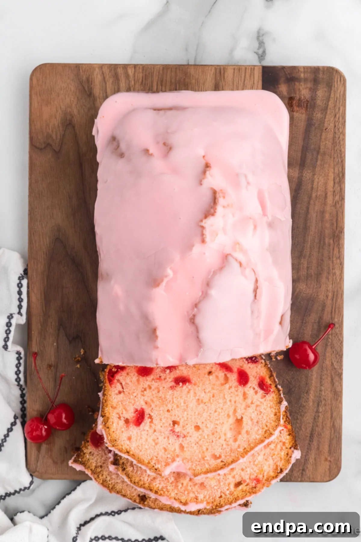 A hand slicing a delicious loaf of Cherry Bread, revealing its tender, cherry-filled interior.
