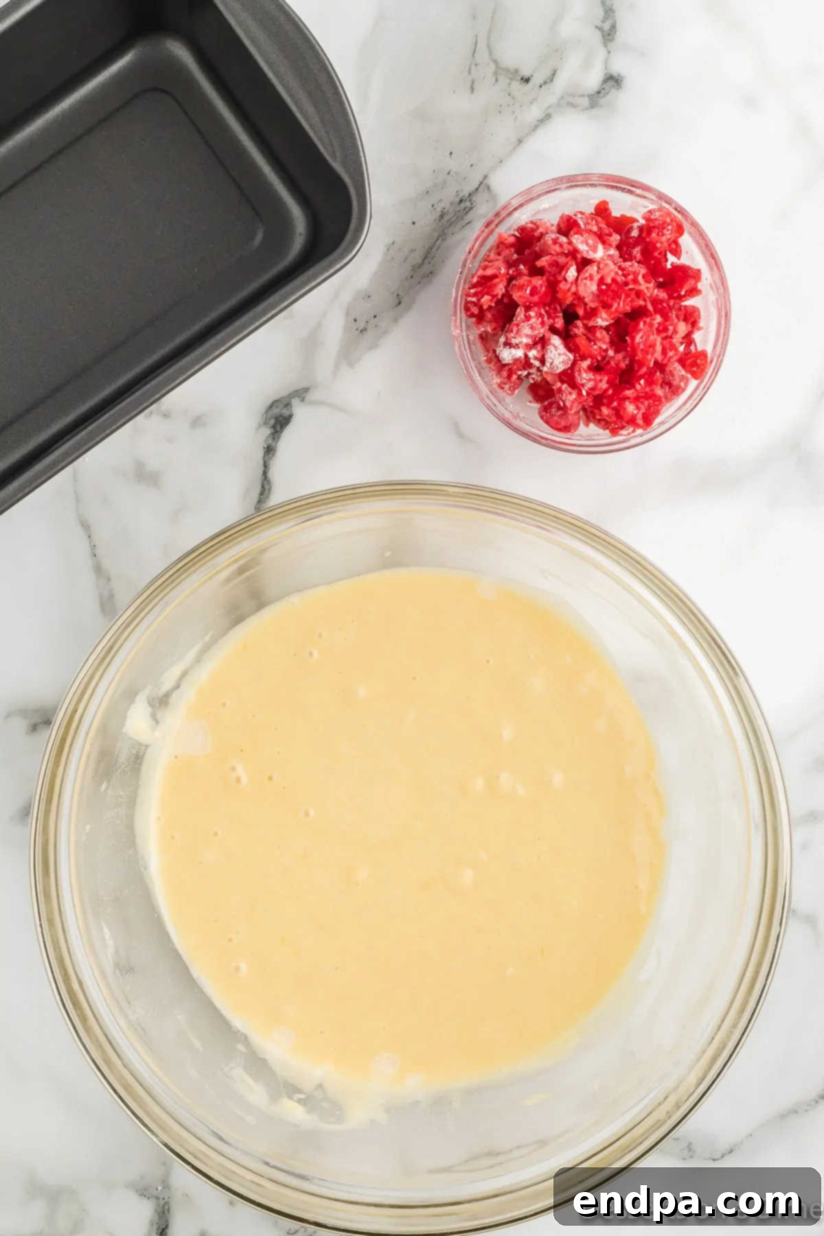 Mixing bowl with wet batter and floured cherries, ready to be gently folded in.