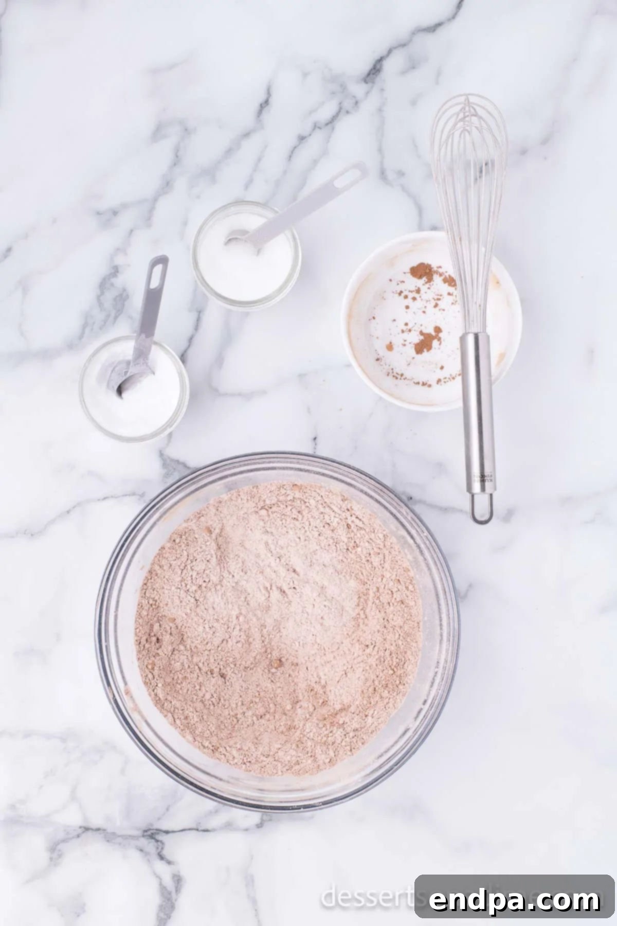 Dry ingredients for cookies, including flour, cocoa powder, baking soda, and salt, are thoroughly whisked together in a large mixing bowl, ensuring even distribution.