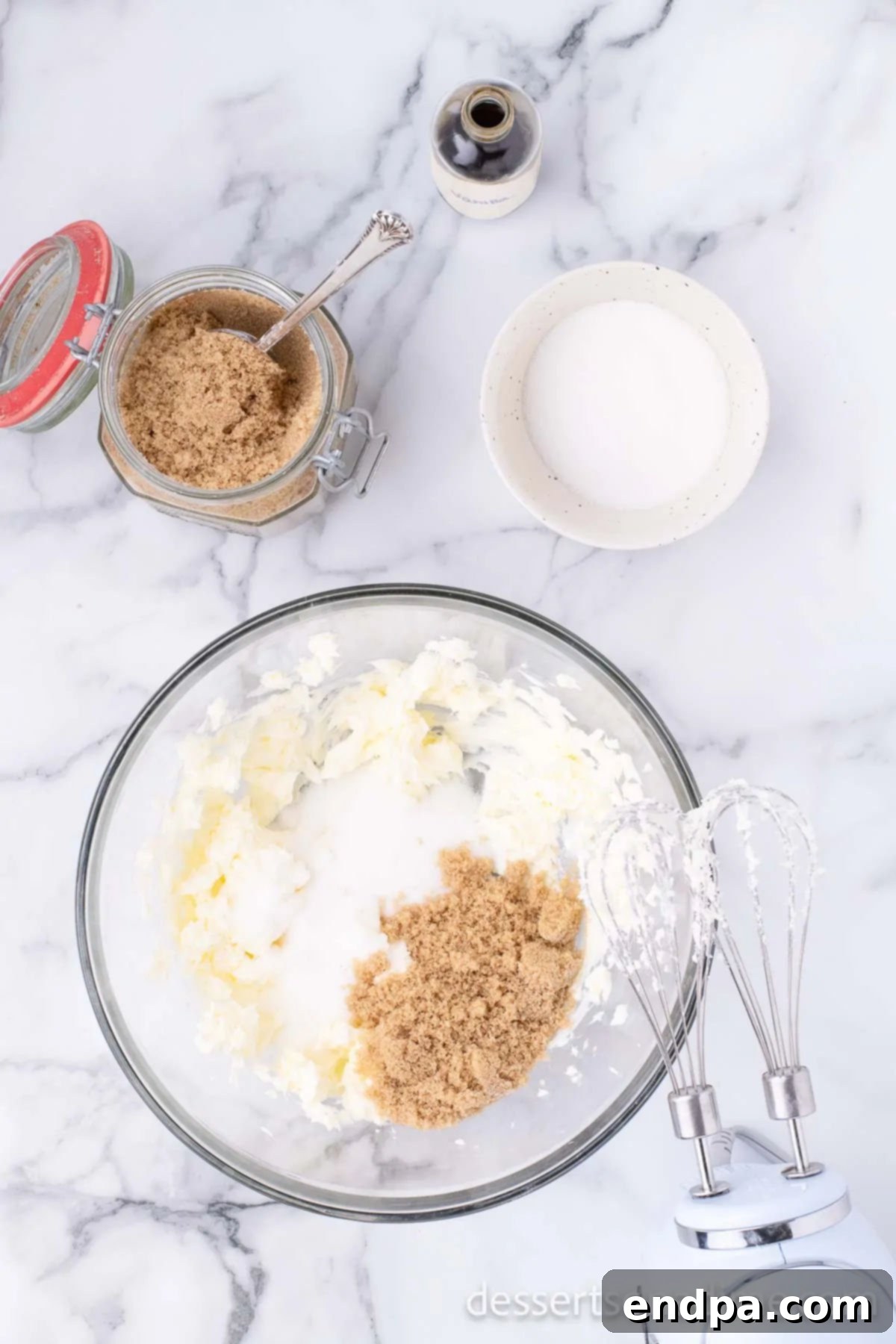 Softened butter, granulated sugar, and brown sugar are creamed together in a bowl using an electric mixer until light, fluffy, and smooth, ready for wet ingredients.
