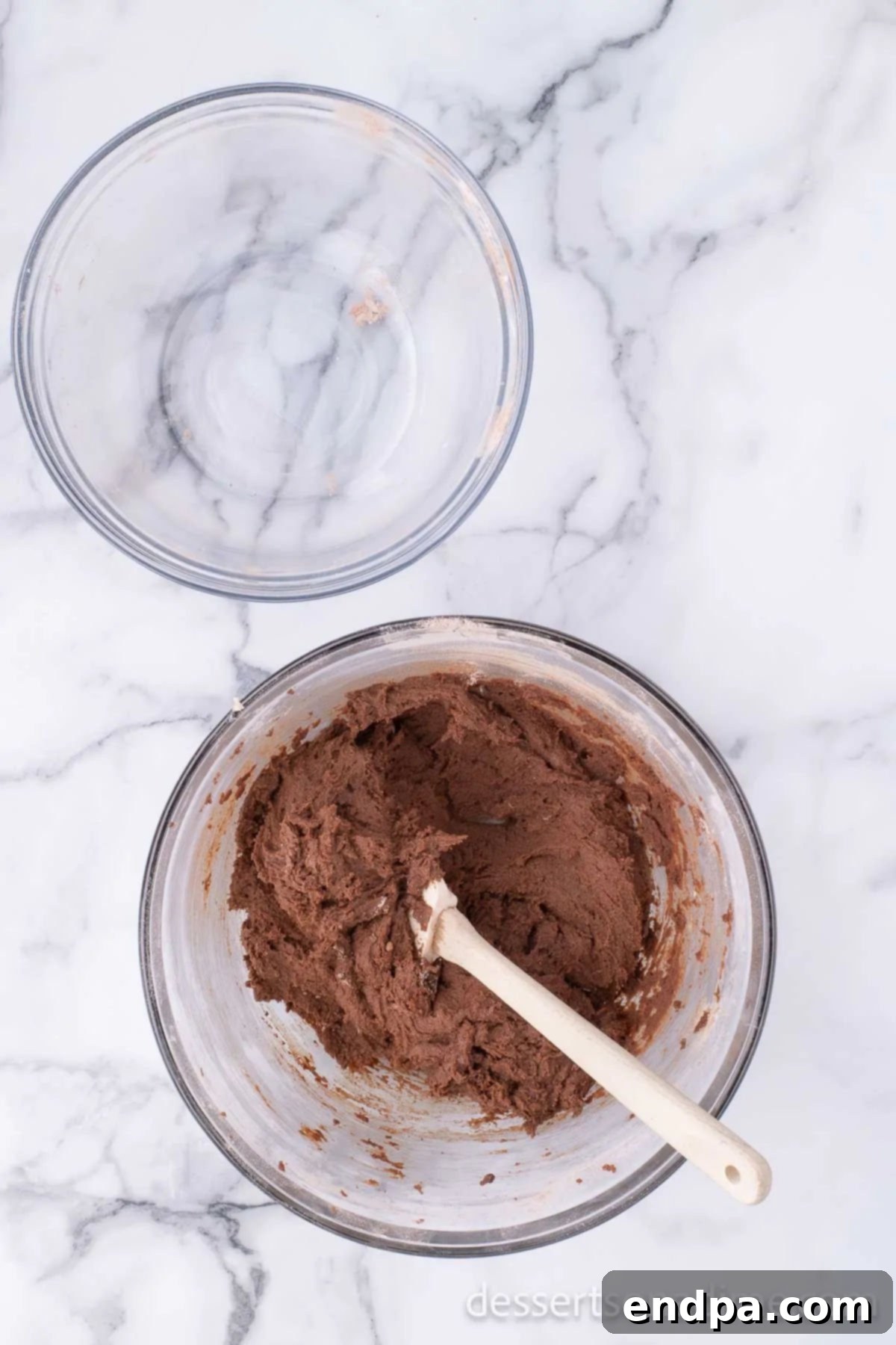 The dry ingredients are gently folded into the wet ingredients in a mixing bowl, creating a cohesive chocolate cookie dough without overmixing.