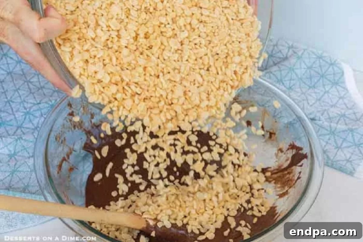 Rice Krispie cereal being poured into the melted chocolate mixture in a bowl.