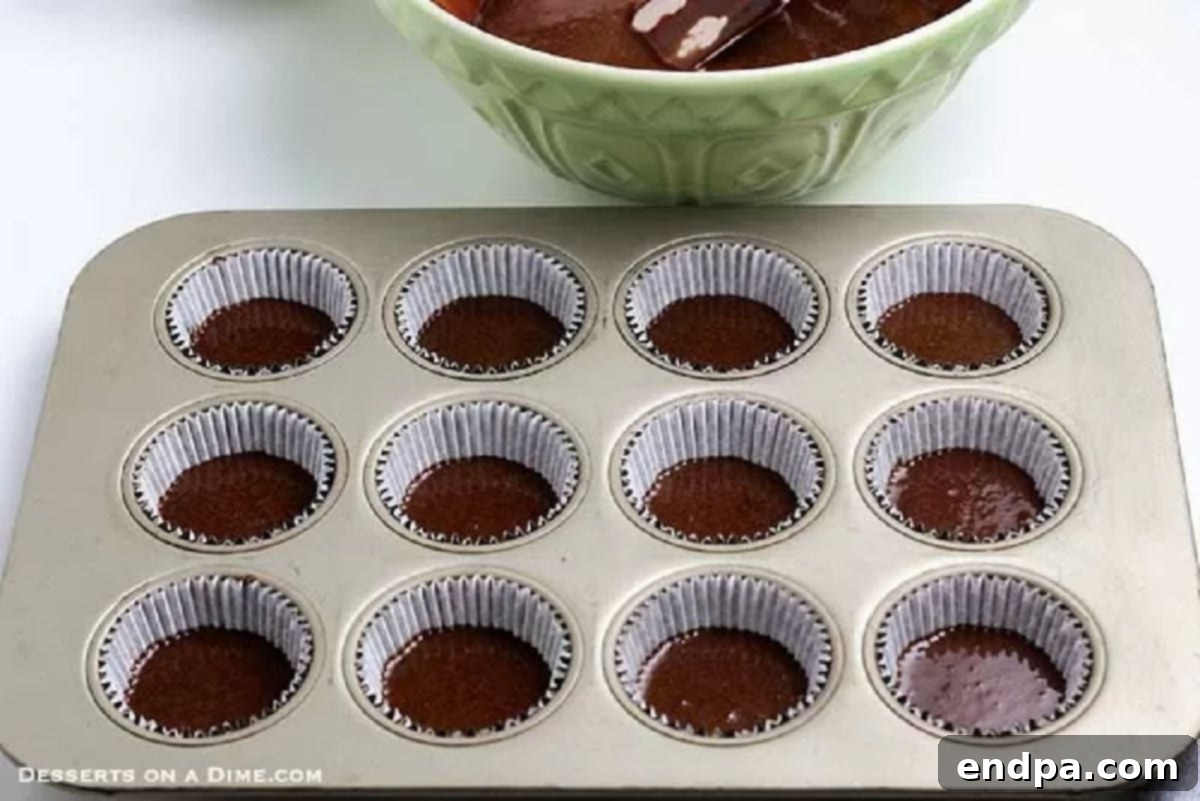Chocolate cupcake batter poured neatly into paper liners in a muffin pan, ready for baking.