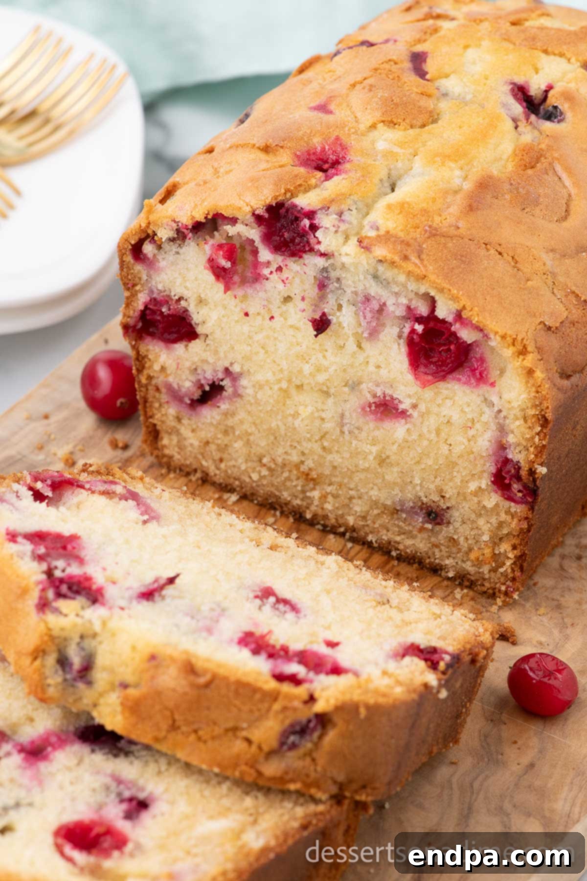 Homemade Sweet-Tart Cranberry Loaf 2 A freshly baked loaf of cranberry bread being expertly sliced on a wooden board, showcasing its moist interior filled with red cranberries.
