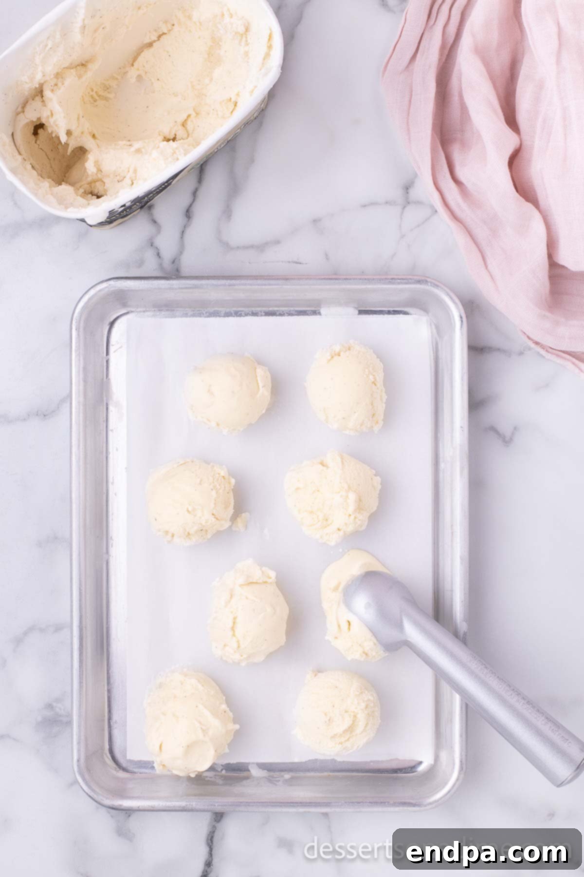 Scoops of vanilla ice cream placed on a baking sheet, ready for freezing.