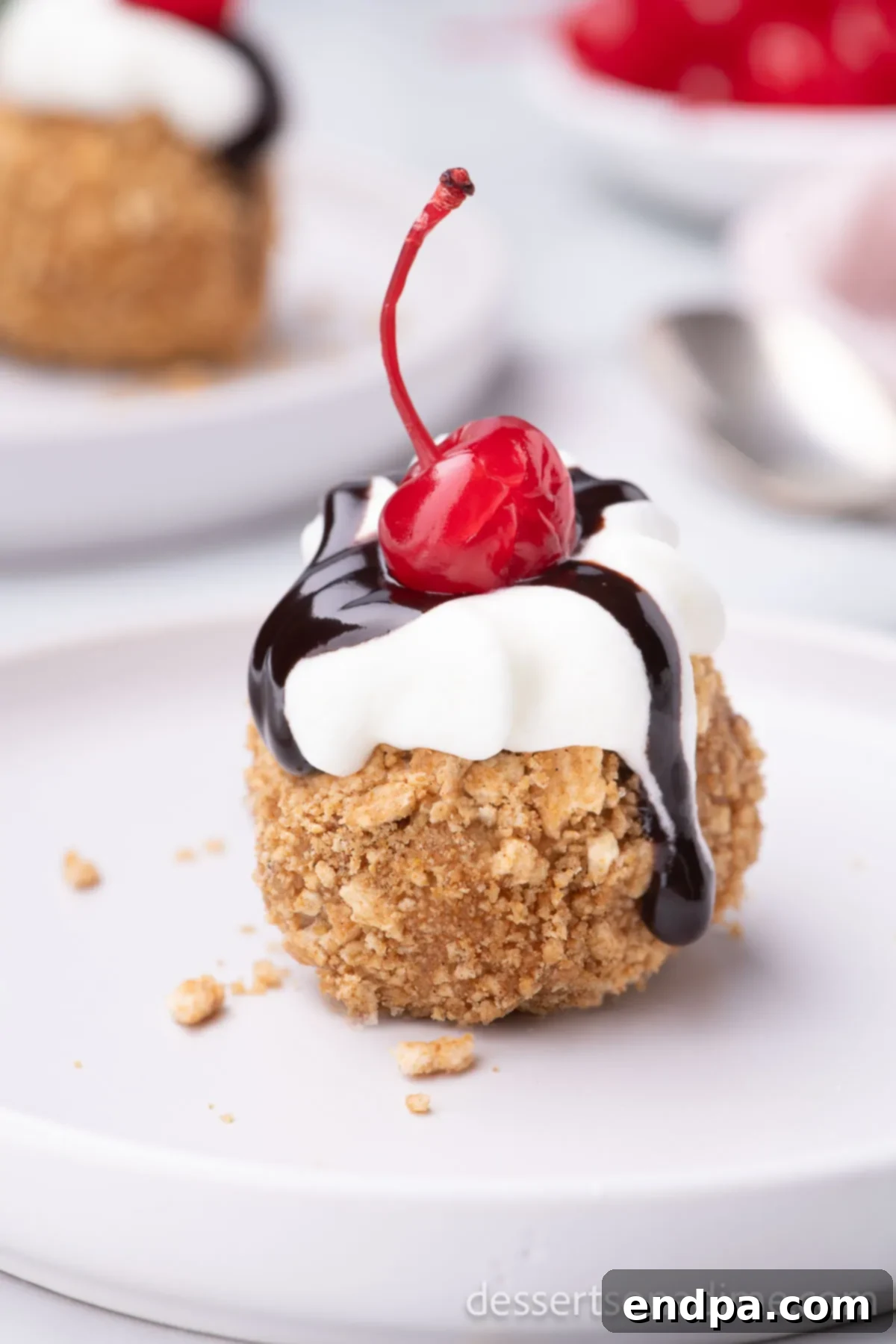 A perfectly air-fried ice cream ball on a plate, generously topped with chocolate sauce, whipped cream, and a cherry.