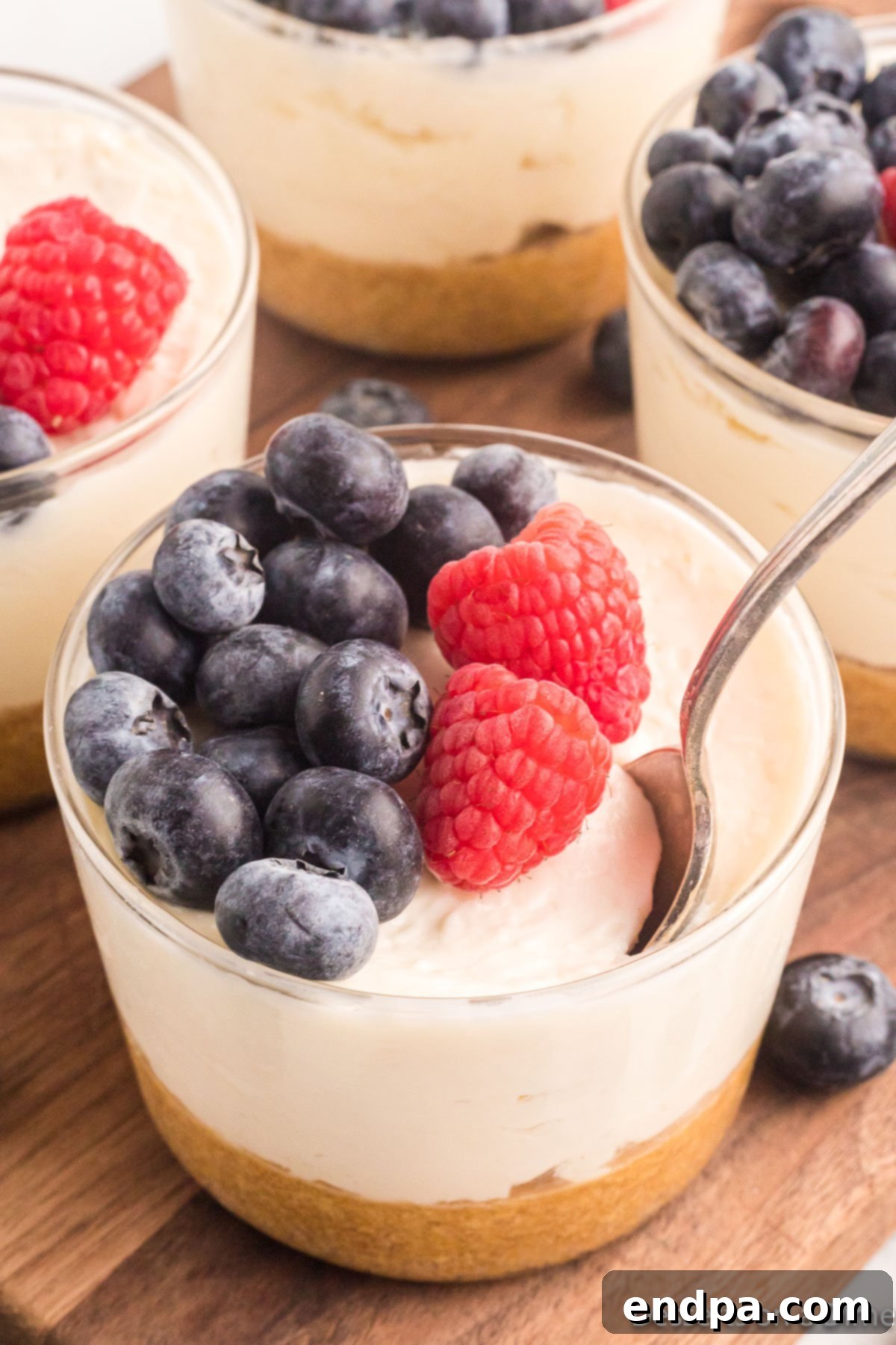 Cup with rich and creamy cheesecake pudding and fresh berries with a spoon in it.
