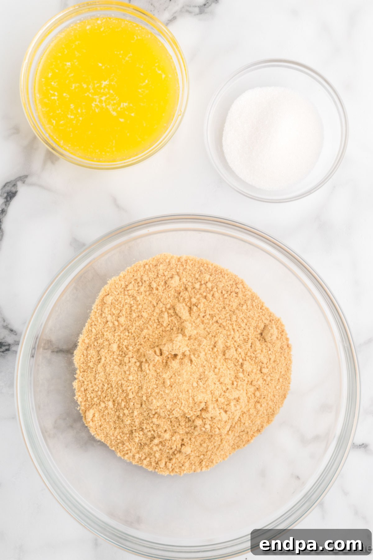 Bowl of graham cracker crumbs beside a bowl of melted butter and bowl of sugar.