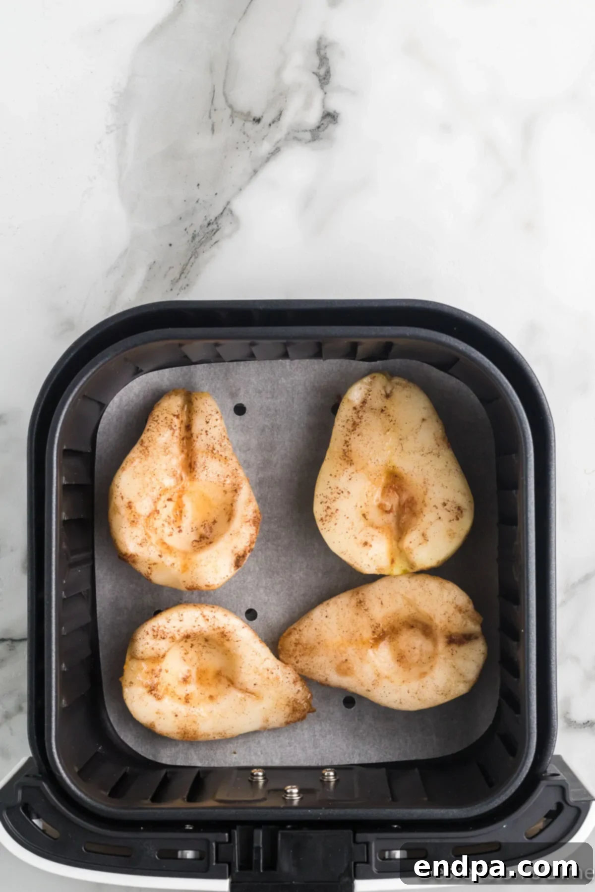 Coated pear halves arranged in a single layer in an air fryer basket.