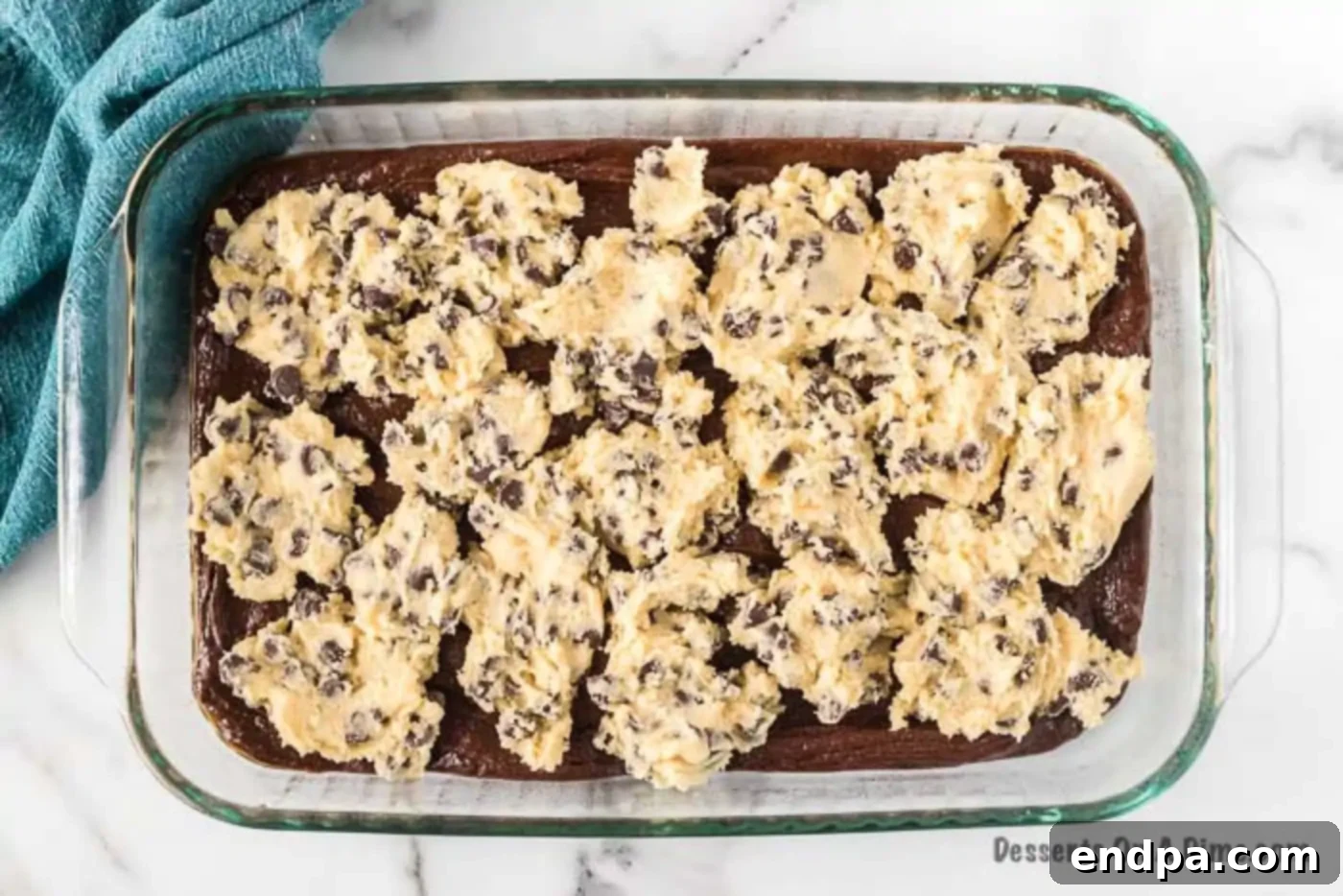 Spoonfuls of cookie dough carefully placed on top of brownie batter in a baking dish.