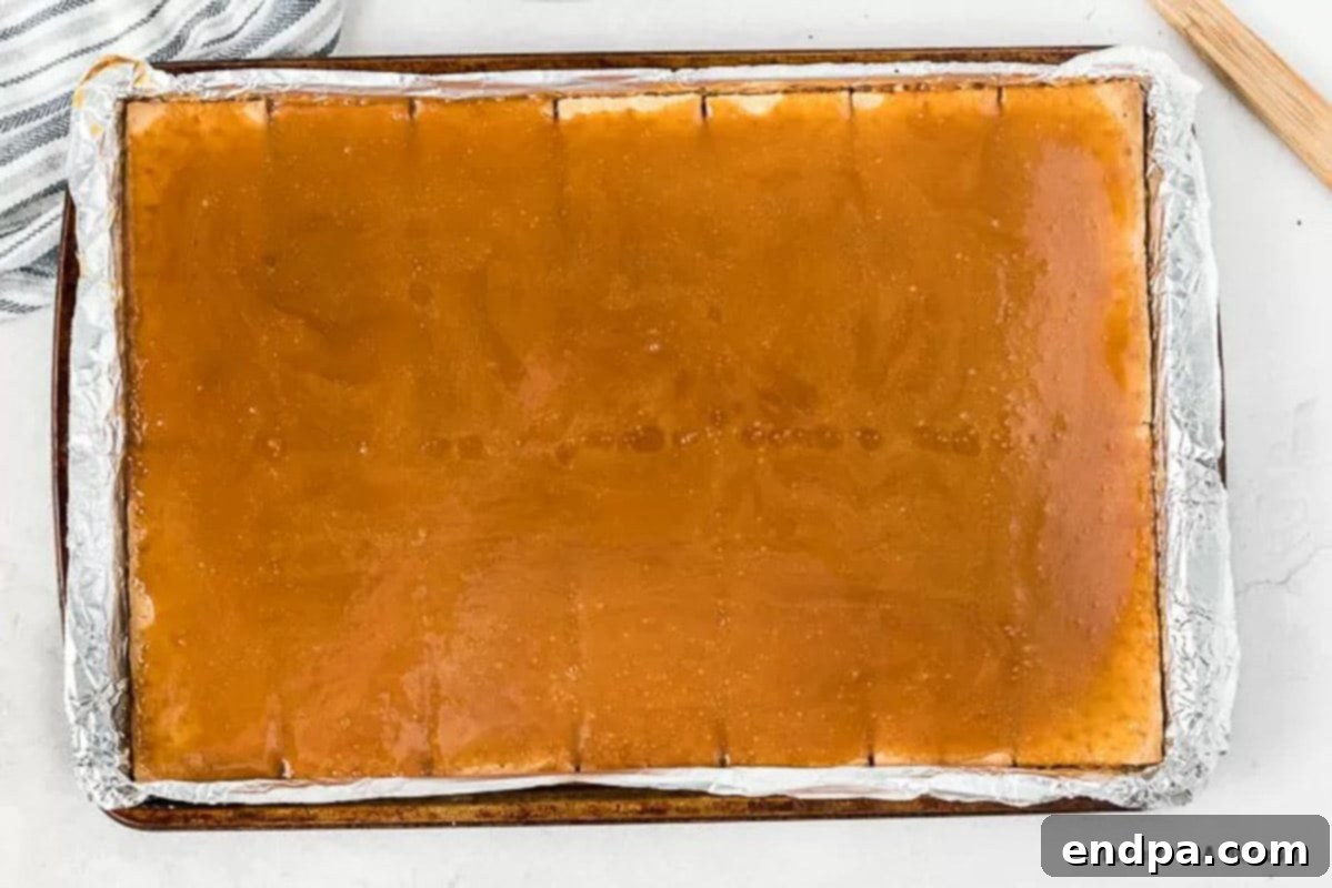 The hot, bubbly brown sugar and butter toffee mixture being poured evenly over the graham crackers in the pan.
