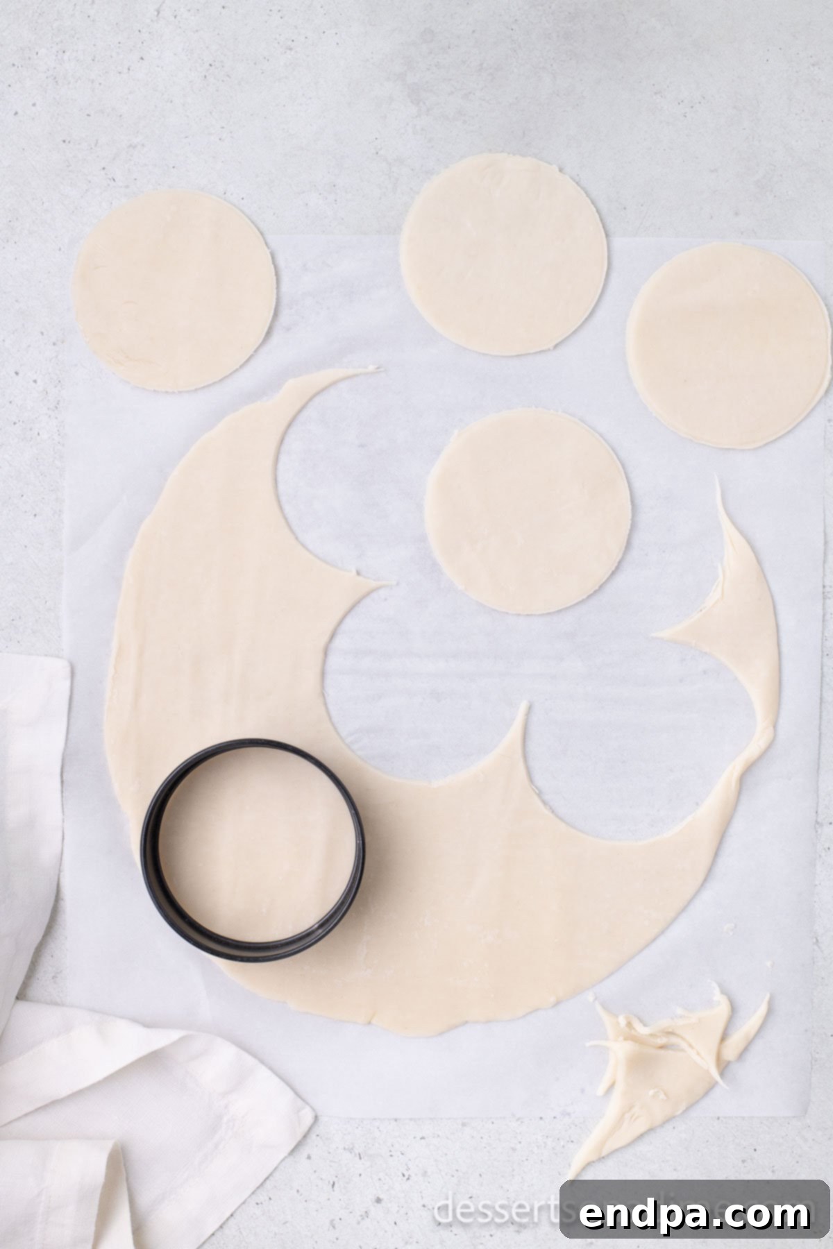 Rolled-out pie crusts with multiple perfect circles cut out using a cookie cutter.