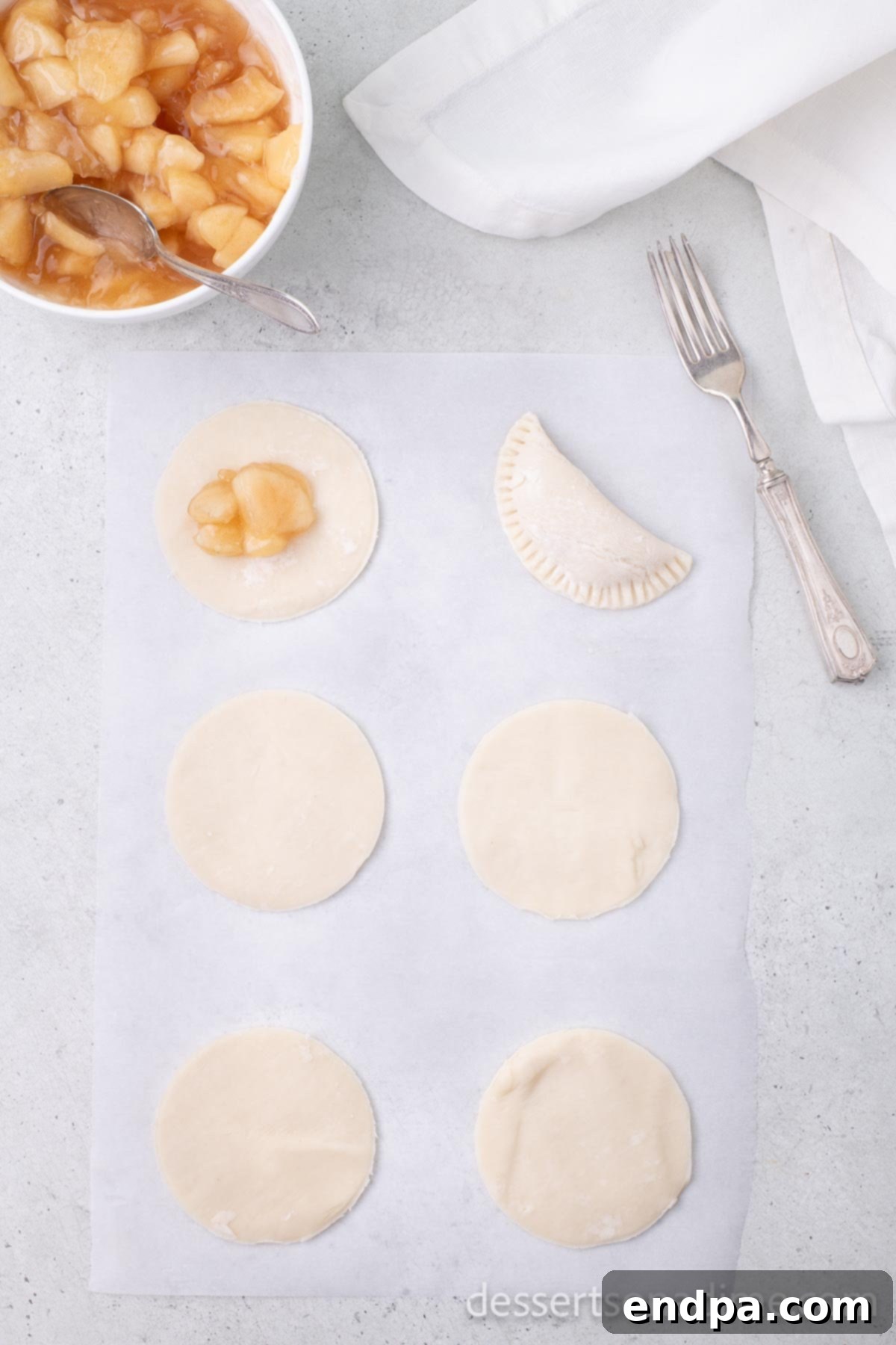 Circular pie dough cutouts with a dollop of apple pie filling placed in the center of each, leaving an edge.