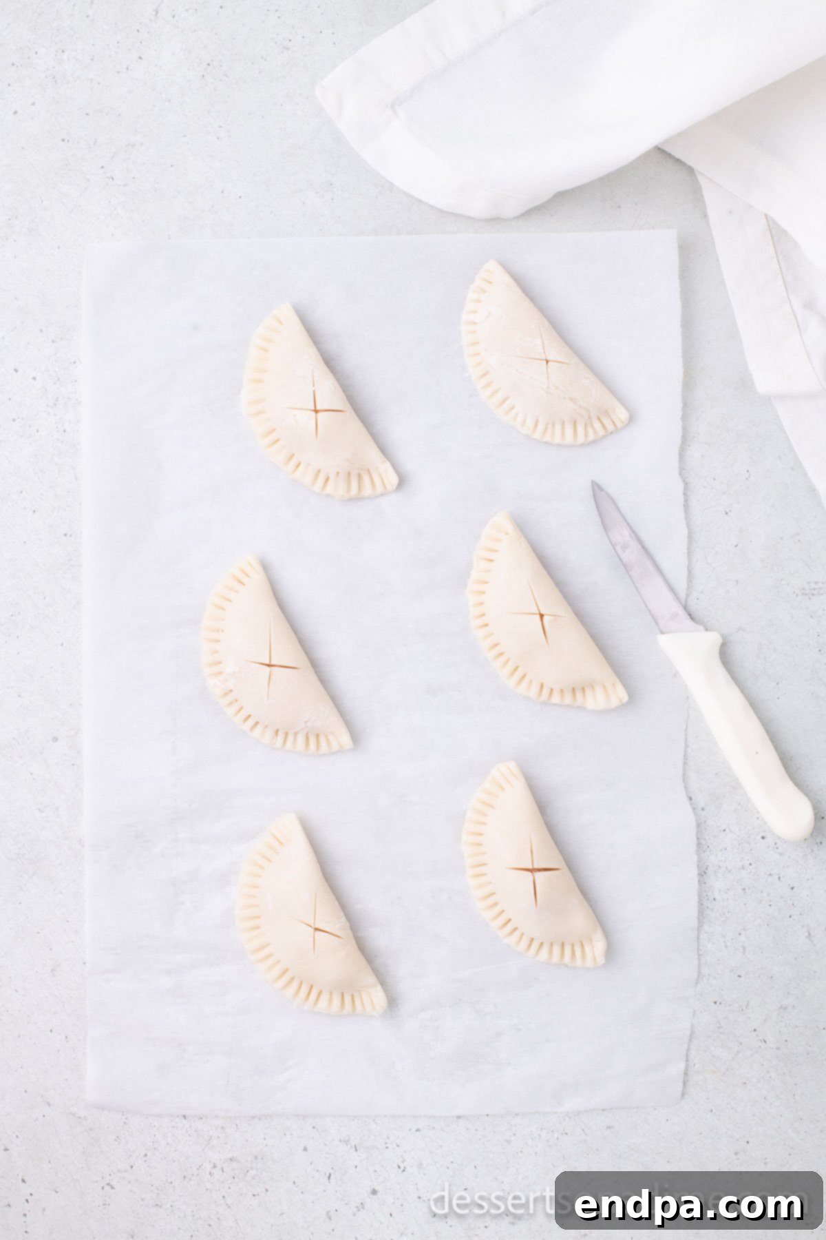 Pie dough folded into half-circles, edges crimped with a fork, and small 'X' slits cut into the top of each.