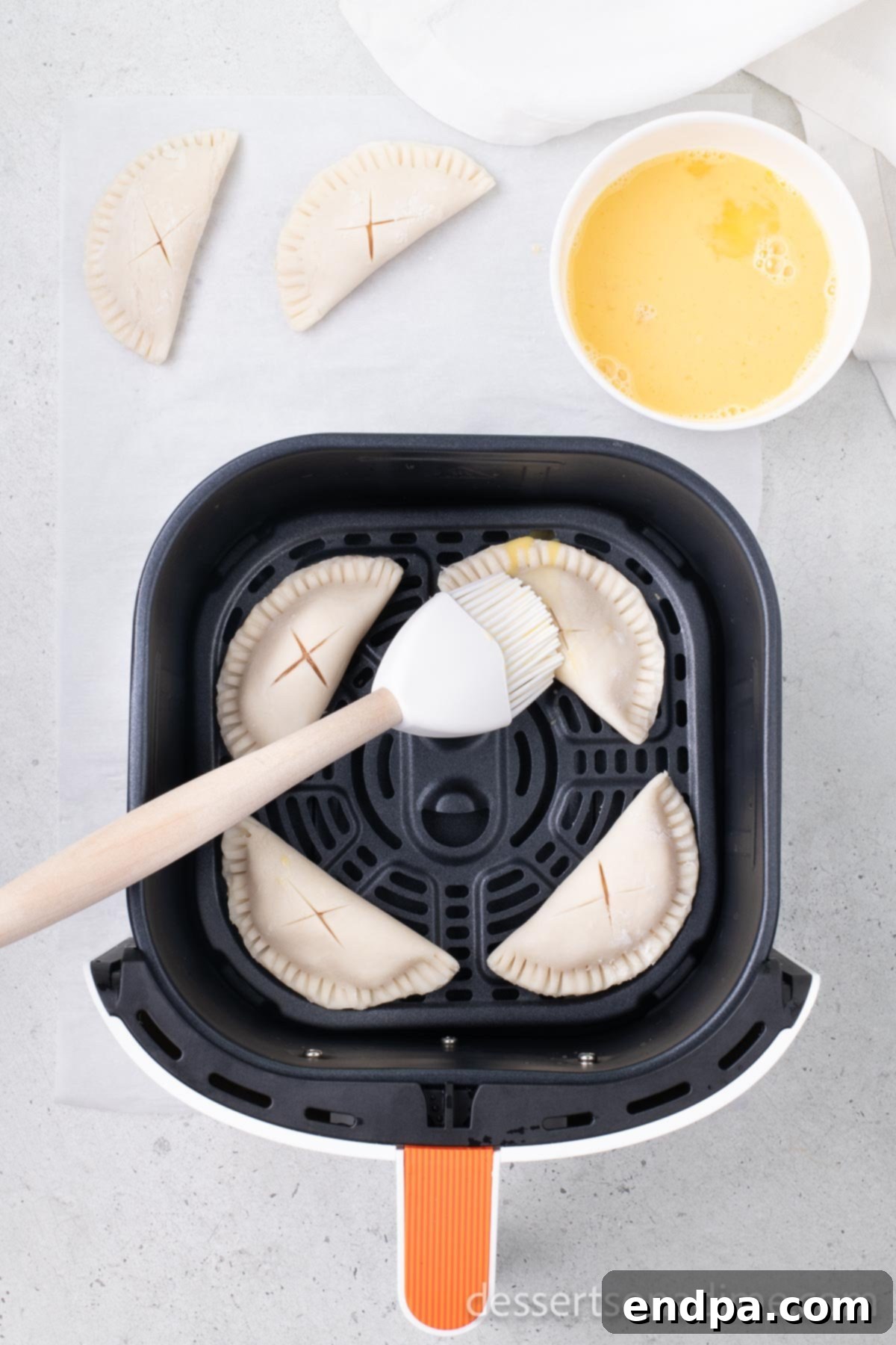 Prepared hand pies arranged in a single layer within an air fryer basket, brushed with egg wash.