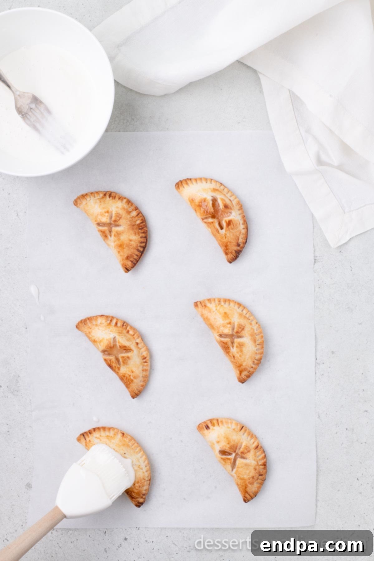 A pastry brush applying a smooth white glaze to the top of a cooled, golden-brown air fryer hand pie.