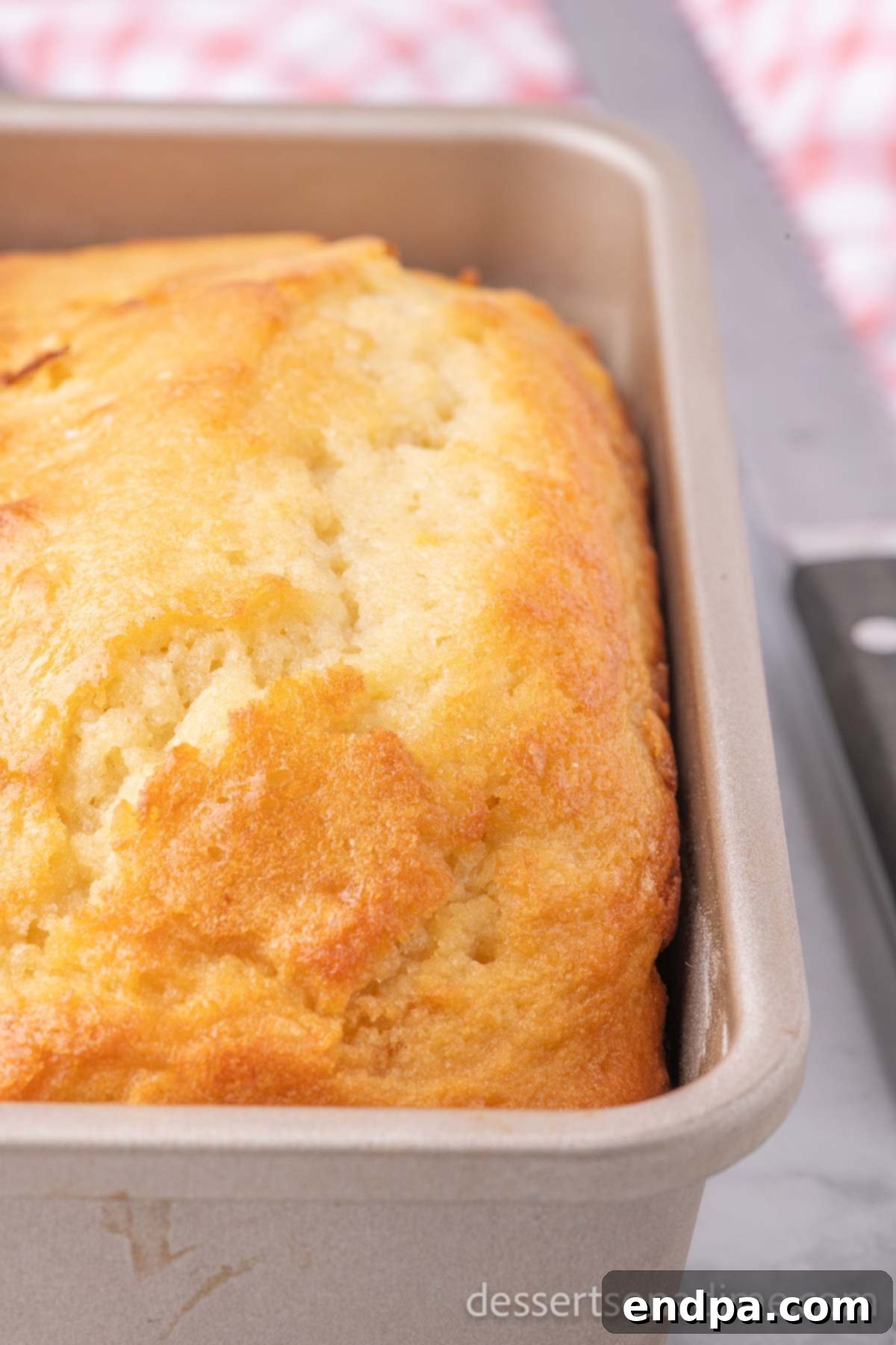 A perfectly golden-brown sweet bread loaf, freshly baked in its pan, cooling slightly before being removed.