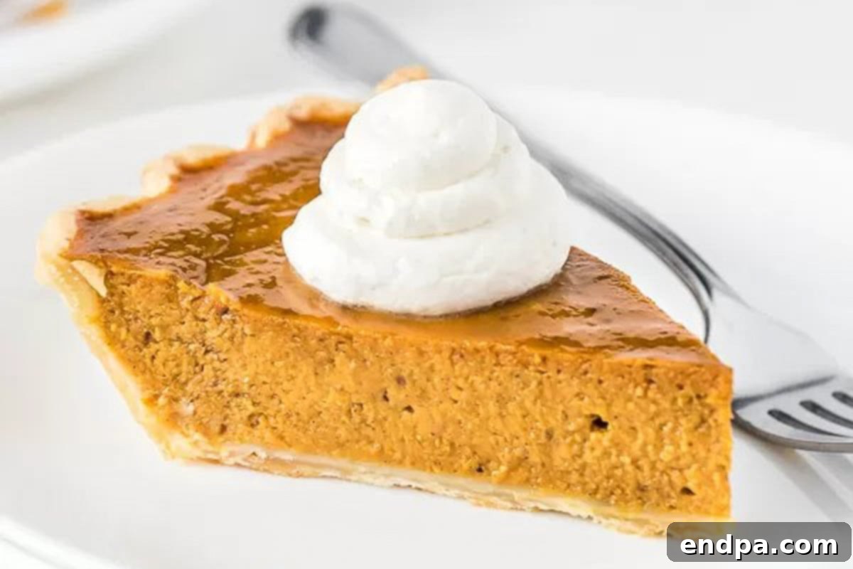 A beautifully sliced pumpkin pie topped with a dollop of homemade whipped cream, ready to be served on a white plate with a fork.