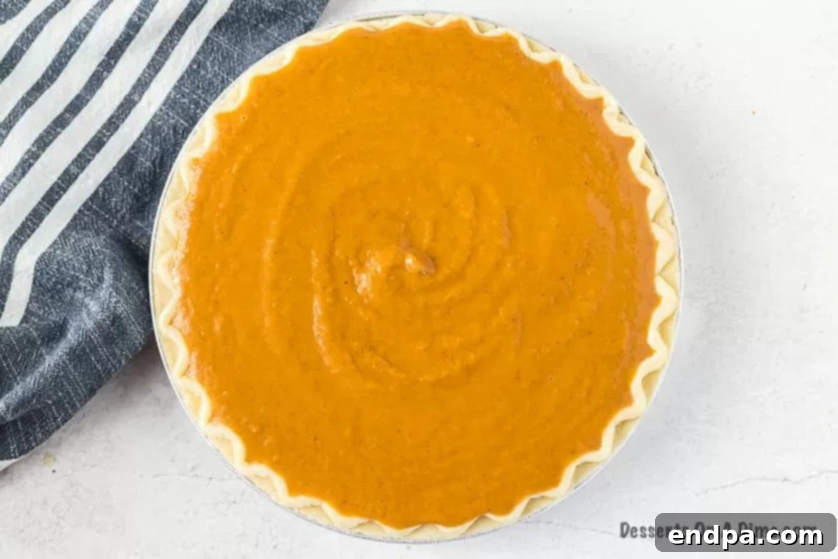 The smooth pumpkin pie filling is carefully poured into an unbaked pie crust set in a pie plate, ready for baking.