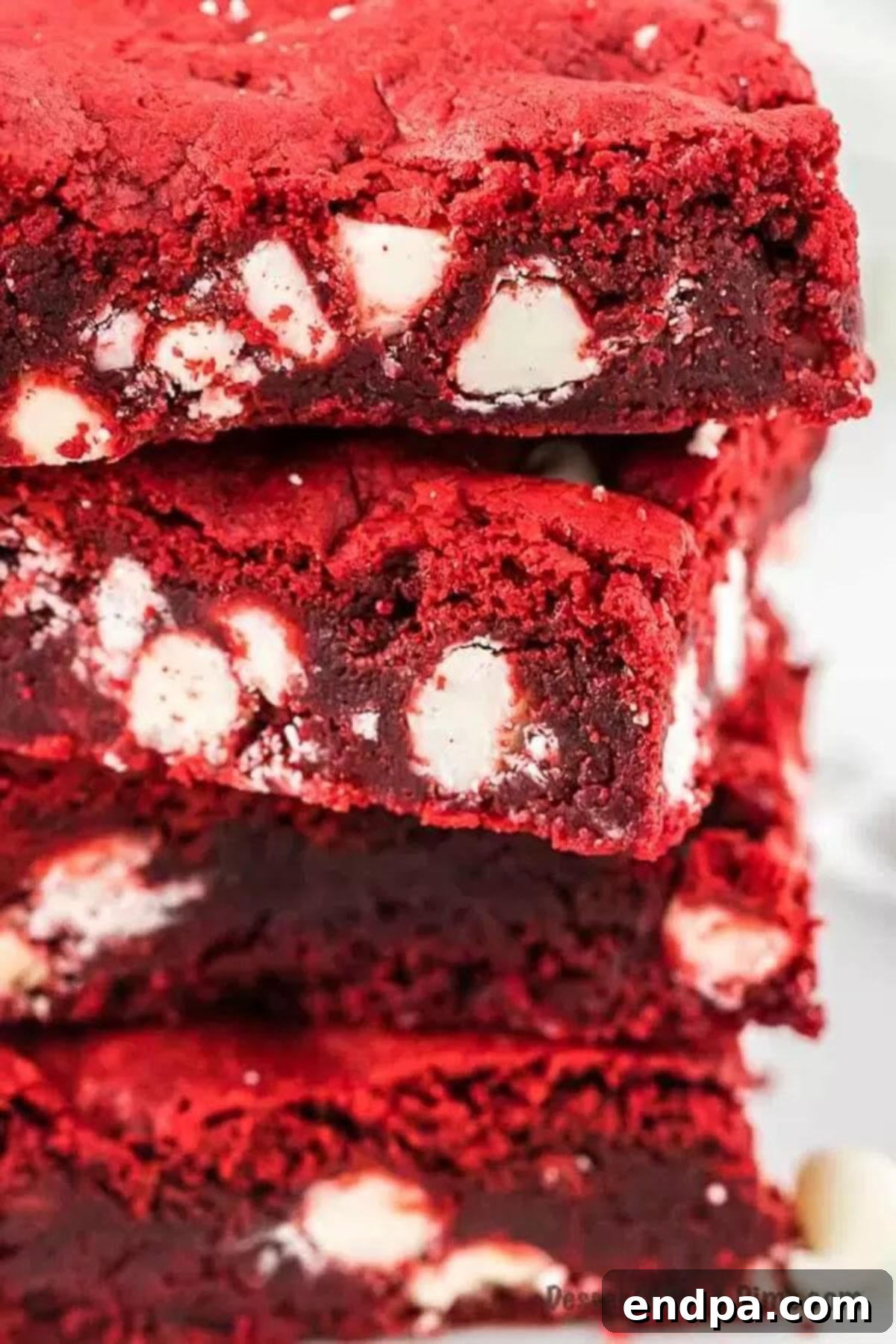 Ruby Red Brownie Bliss 2 Close up of Red Velvet Brownies stacked on top of each other, showcasing their vibrant red color and white chocolate chips.