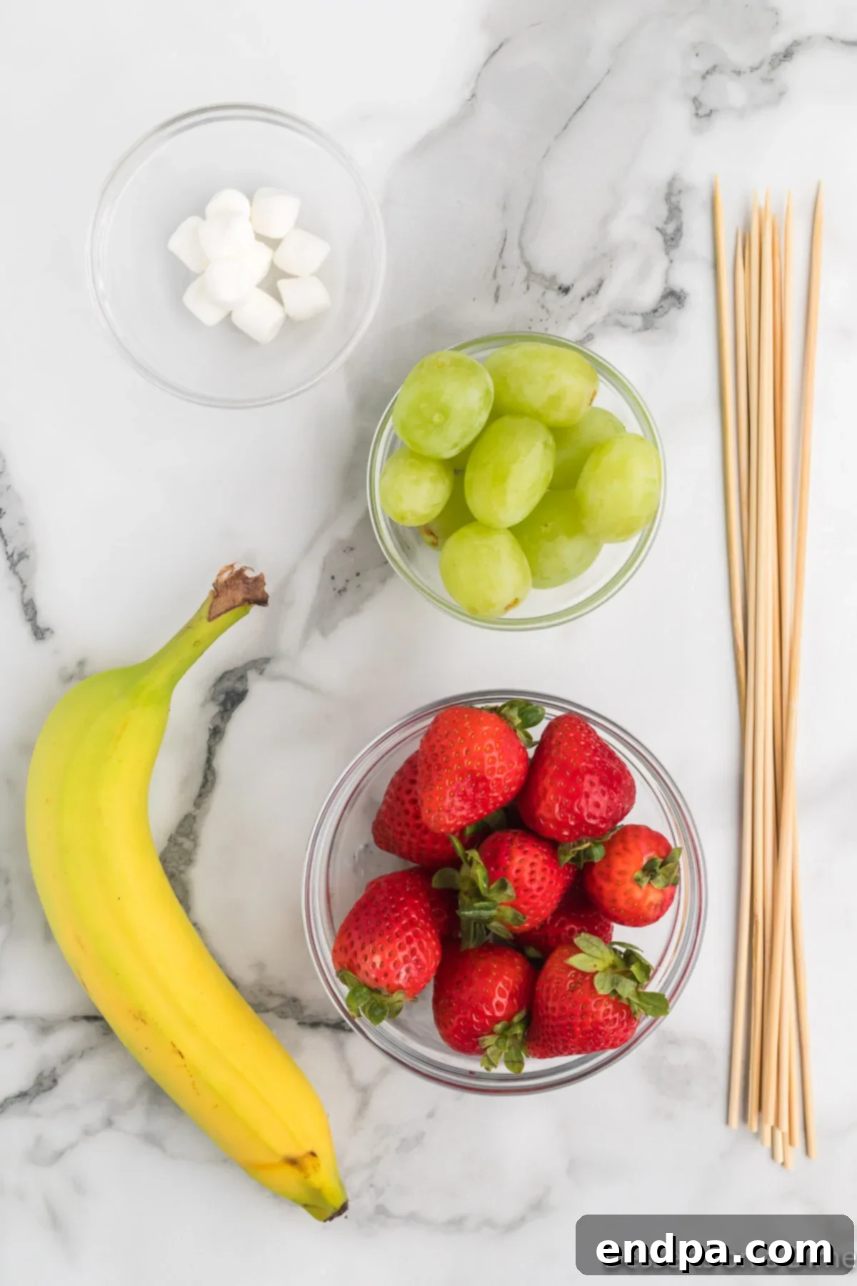 Ingredients for Grinch Fruit Skewers laid out: fresh bananas, green grapes, ripe strawberries, and fluffy mini marshmallows.