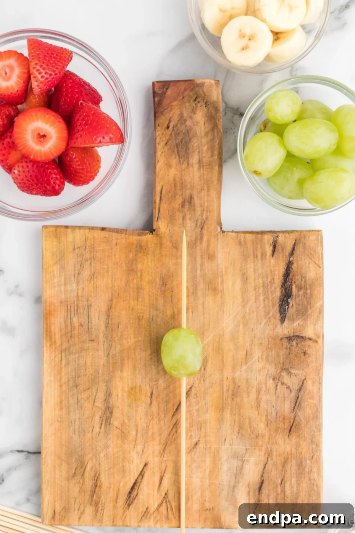A single green grape carefully threaded onto the bottom of a wooden skewer.