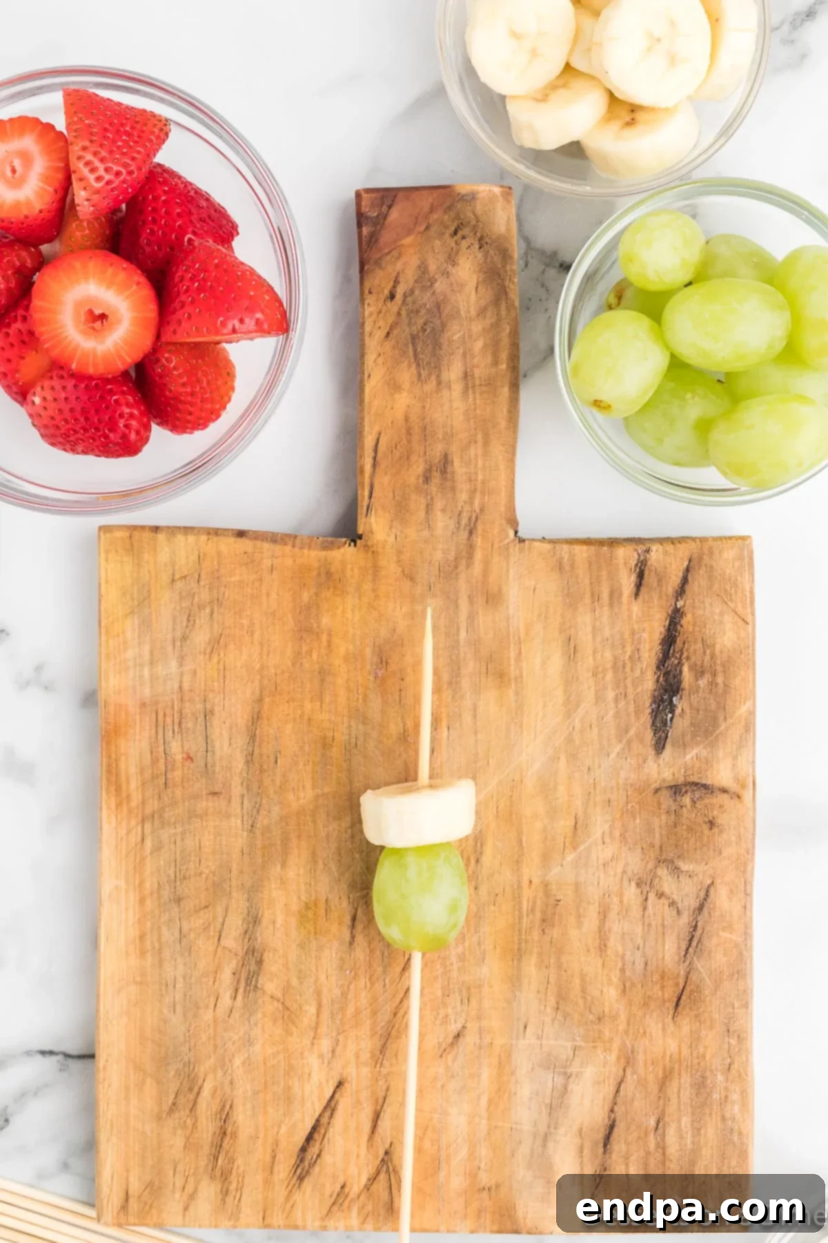 A banana slice placed directly on top of the green grape on a skewer, forming the Grinch's face.