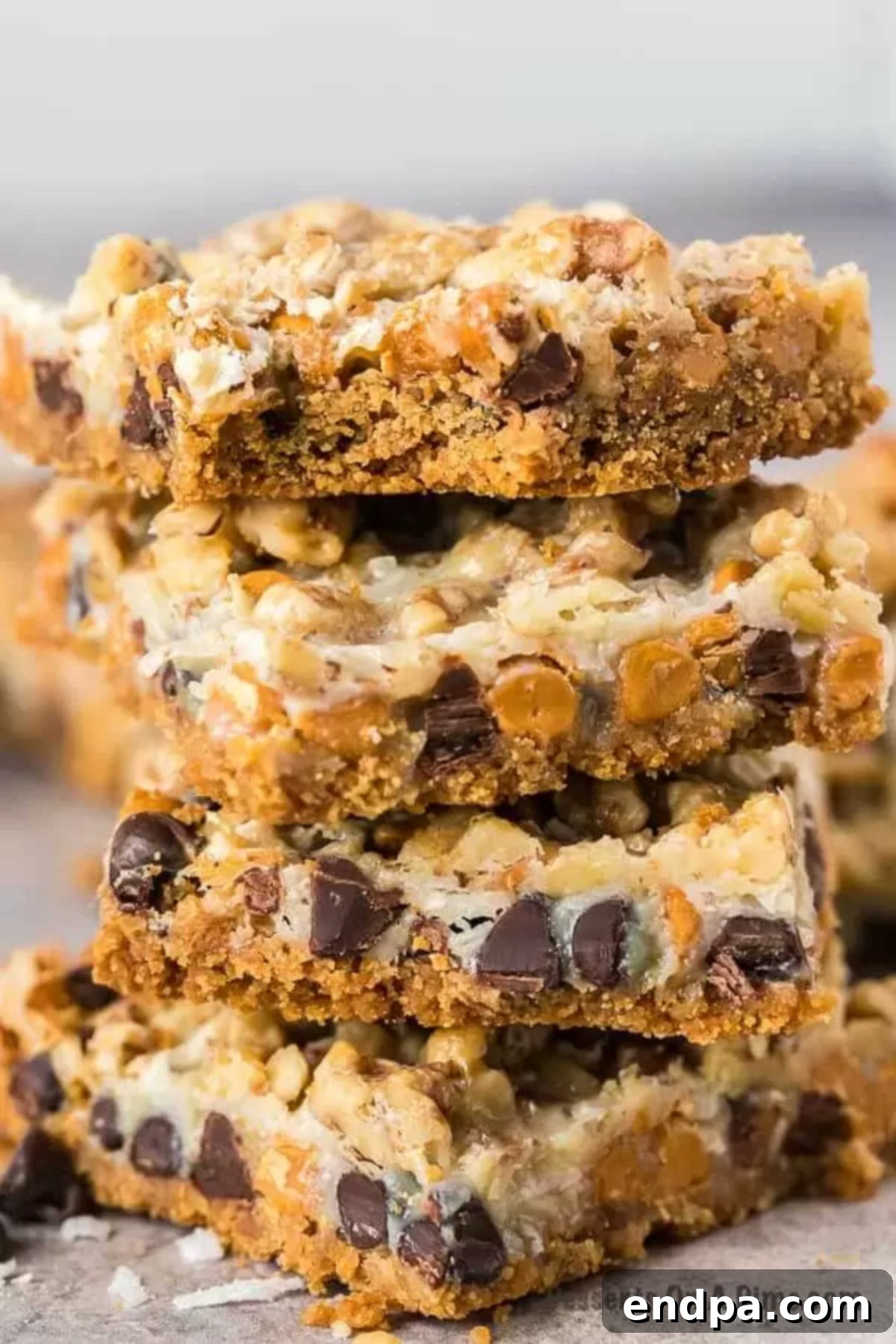 Enjoy decadent layers of chocolate chips, butterscotch, nuts and more in this Magic cookie bars recipe. Each bite is heavenly. Magic Cookie bar cookies are perfect for Christmas, 4th of July and more. Seven layer bars are easy and the best dessert with butterscotch. Everyone will love the 7 layer recipe. #dessertonadime #magiccookiebarsrecipe #eaglebrand #7layer Stack of freshly baked and sliced Magic Cookie Bars on a white plate