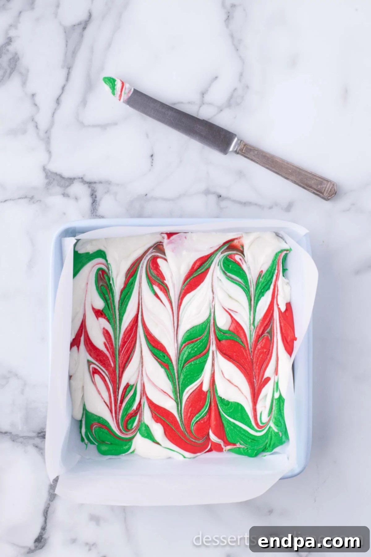 A knife gently creating swirl patterns in the multi-colored fudge mixture.