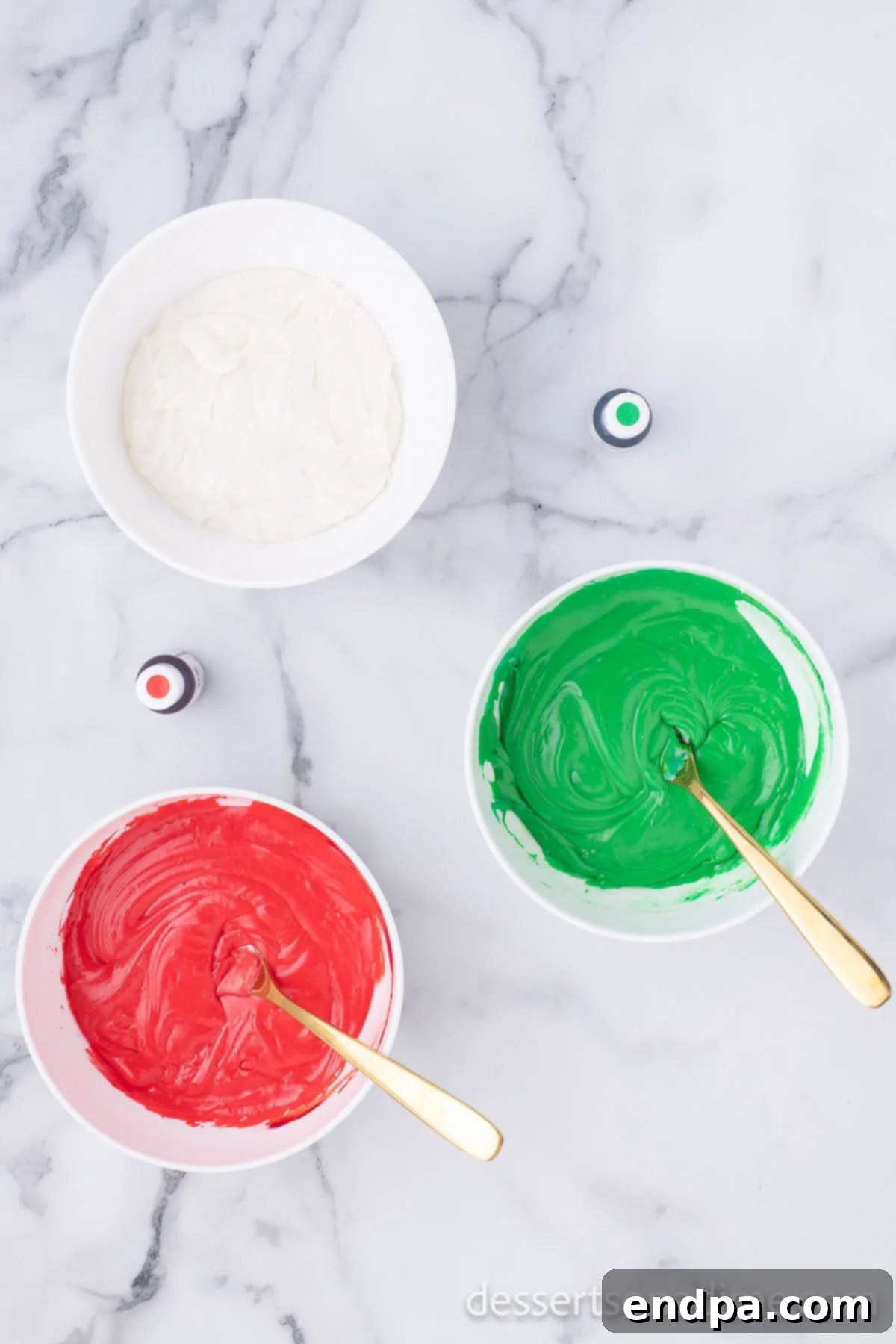 Two bowls of fudge mixture with red and green food coloring added, one bowl remains white.