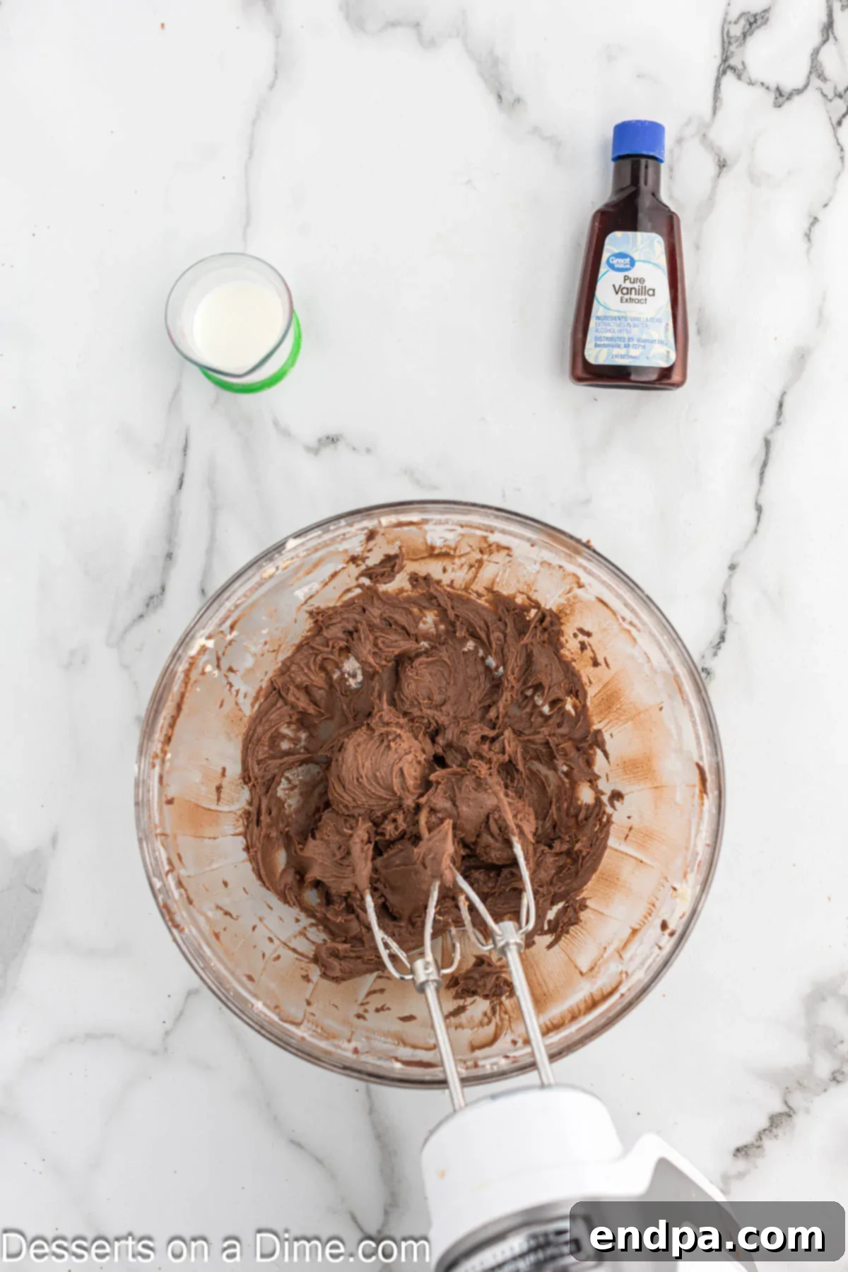 Mixing bowl with ingredients for chocolate cream cheese icing: cream cheese, butter, powdered sugar, cocoa powder, vanilla, and milk.