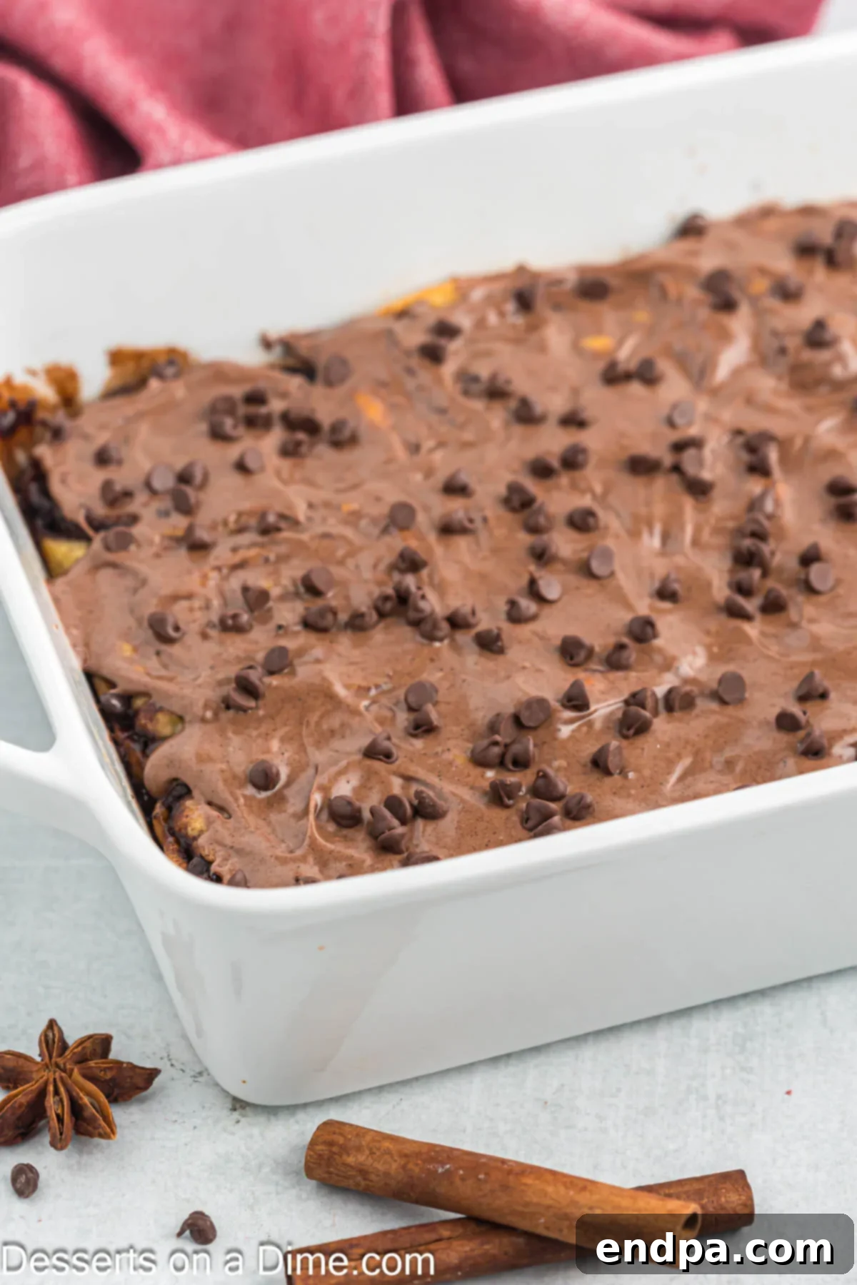 Baked chocolate chip cinnamon rolls in a baking dish, generously covered with chocolate cream cheese icing.