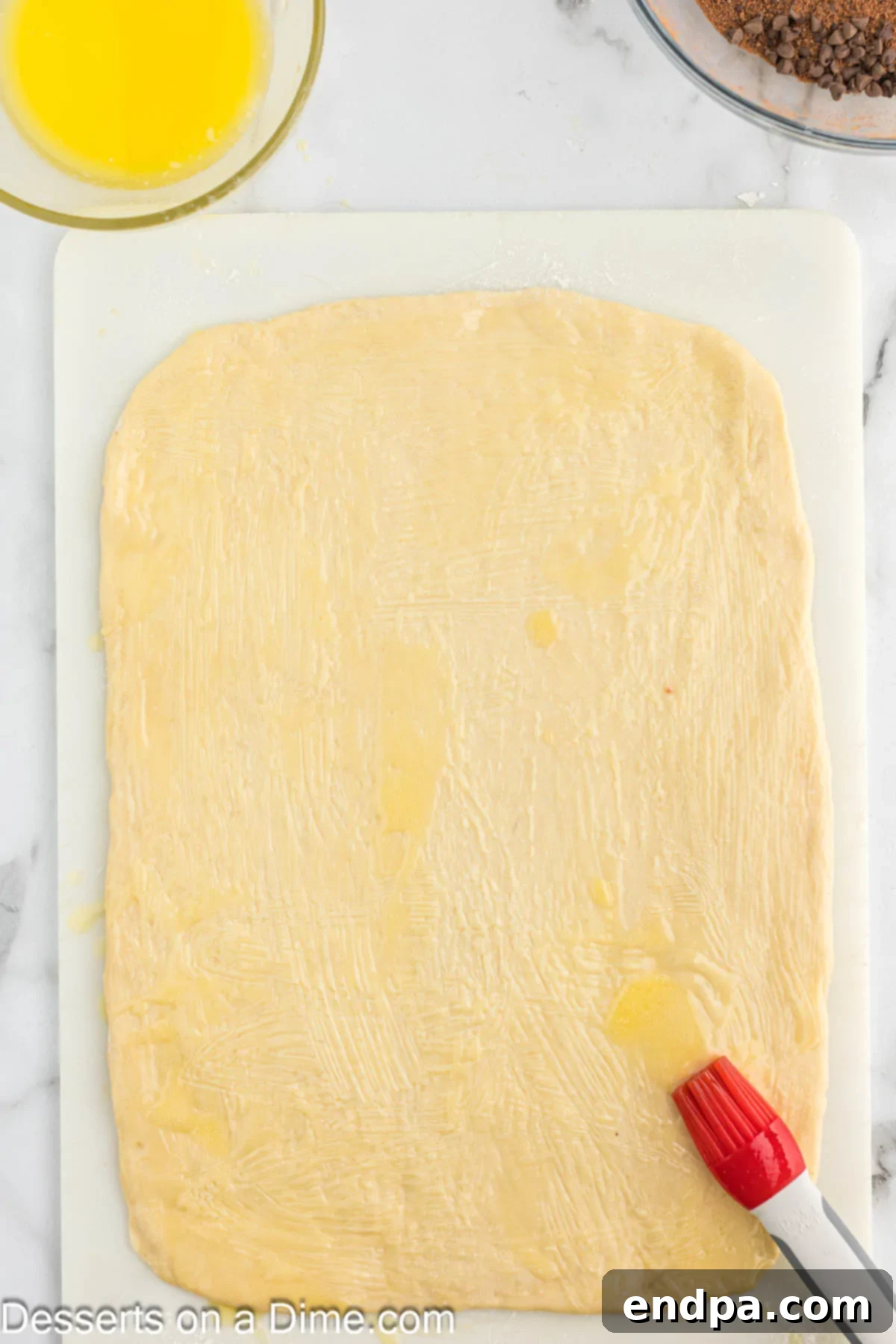 Melted butter being brushed over the surface of the rolled-out dough.